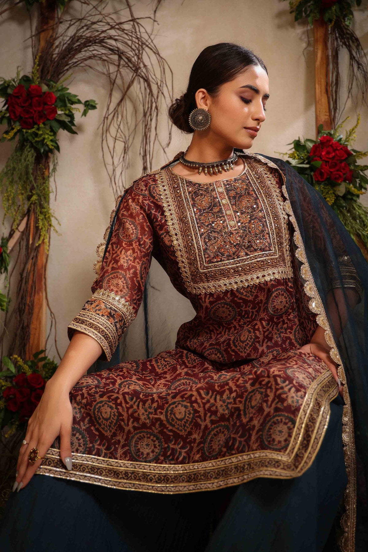 Woman wearing a traditional outfit with intricate patterns in a decorative setting.