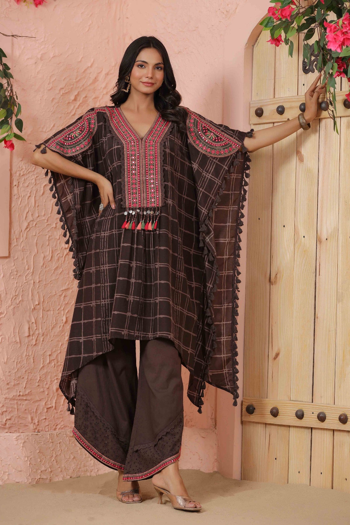 Woman wearing a traditional outfit with a checkered pattern and embroidered details, standing against a wooden door.