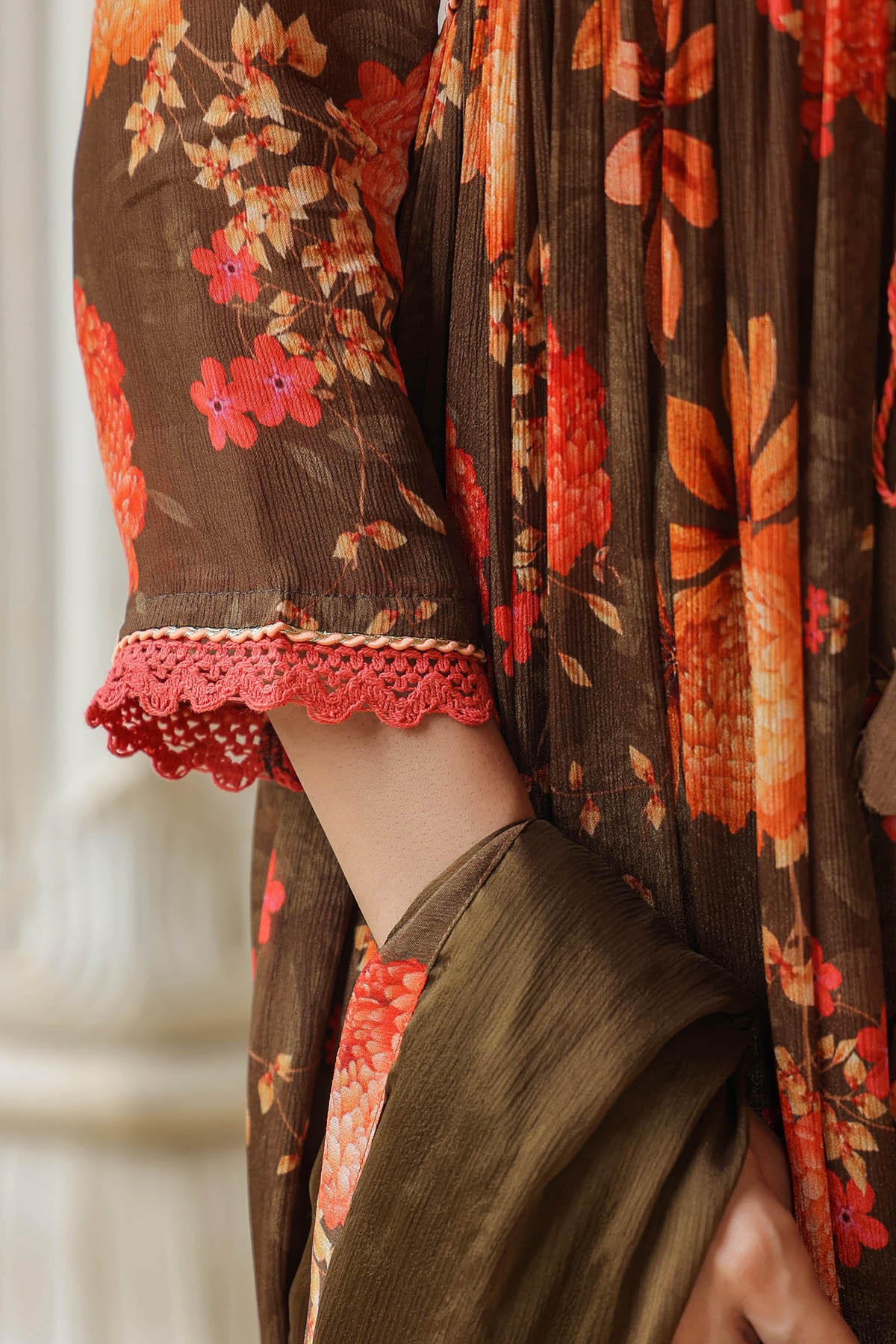 Close-up of a person wearing a brown garment with floral patterns and red lace trim.