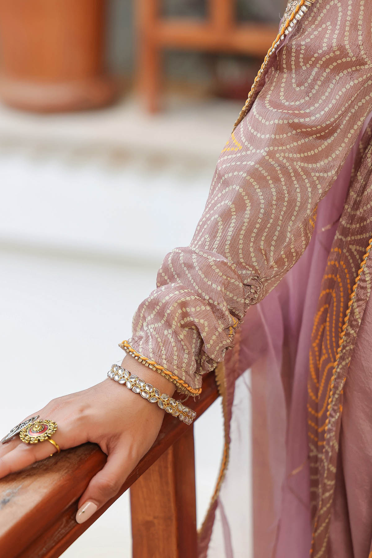 Close-up of a hand wearing a ring and bracelets, with a patterned garment in the background.