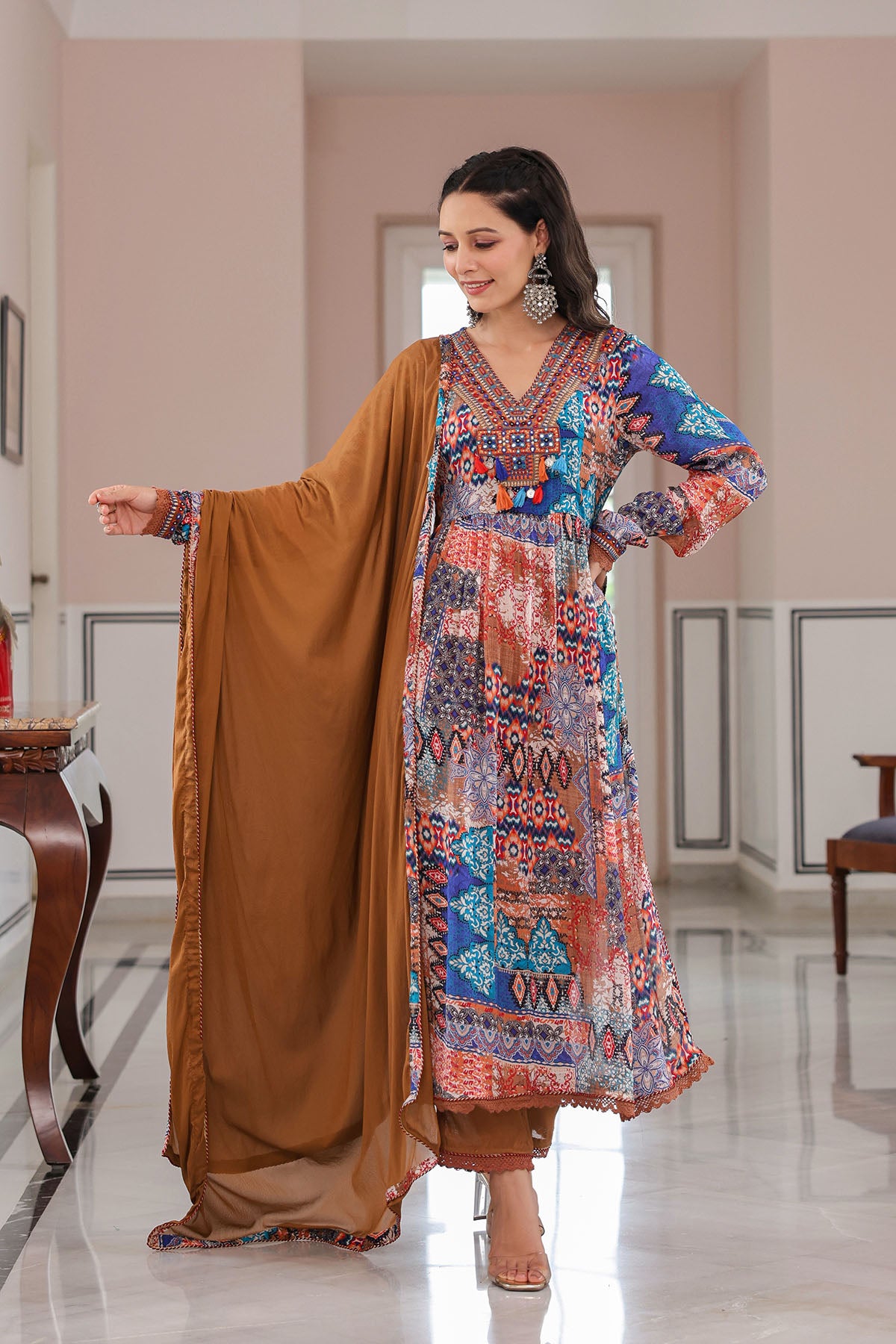 Woman wearing a colorful traditional outfit with a brown dupatta in a well-lit room.