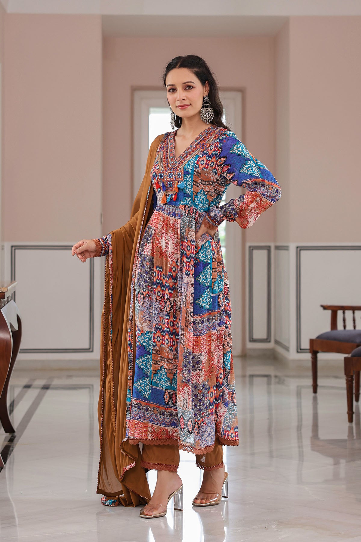 Woman wearing a colorful patterned dress with a brown dupatta in an indoor setting.