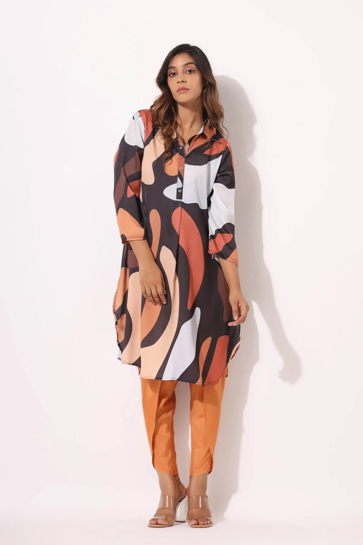 Woman wearing a patterned dress with orange pants on a white background