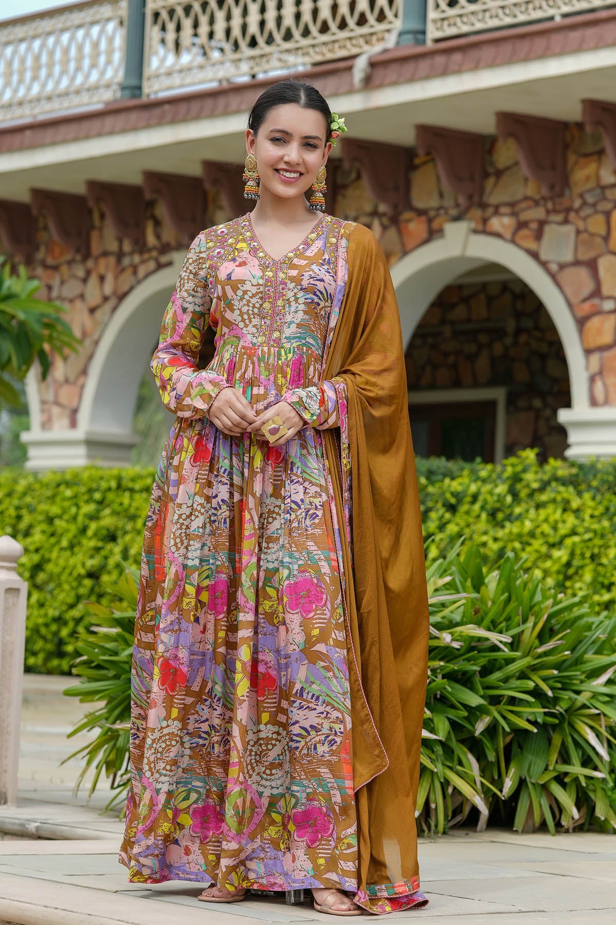 Woman wearing a colorful floral dress and brown dupatta outdoors.