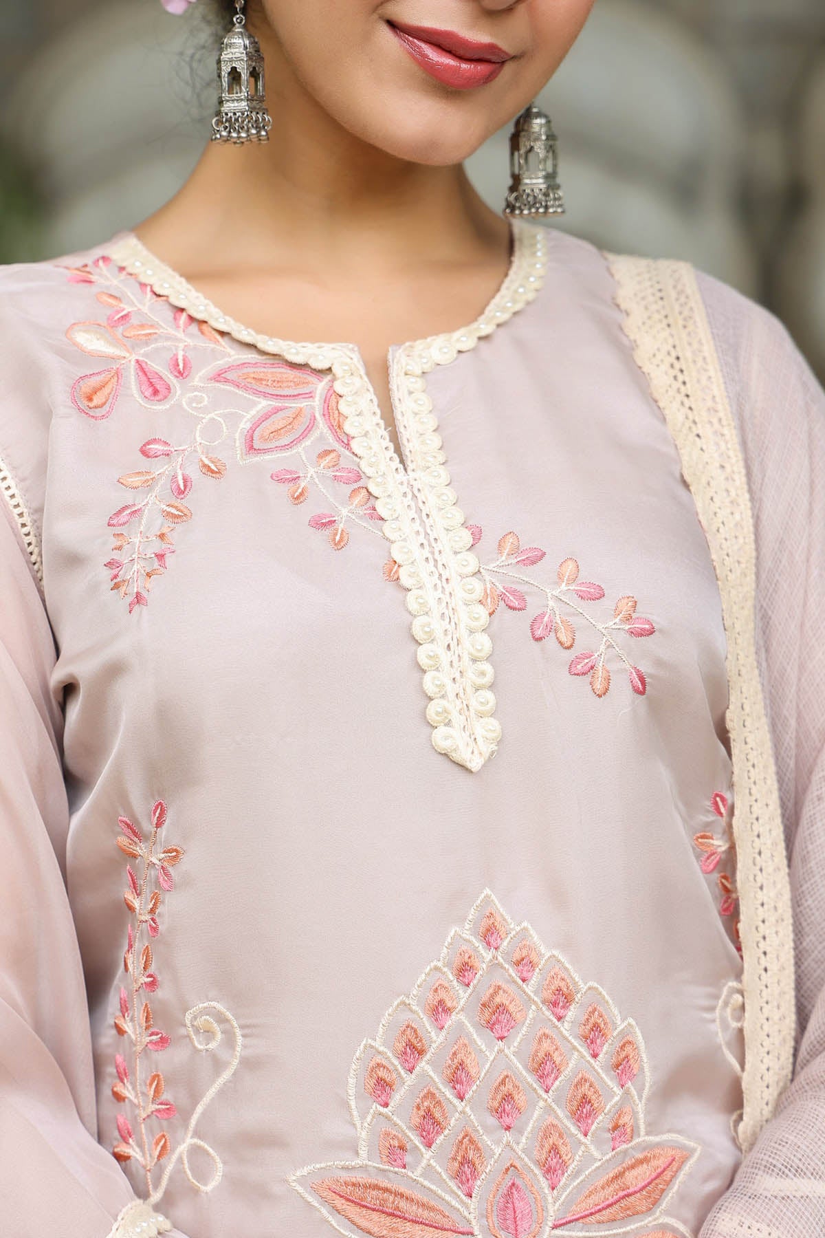 Close-up of a person wearing a light gray embroidered outfit with pink floral patterns.