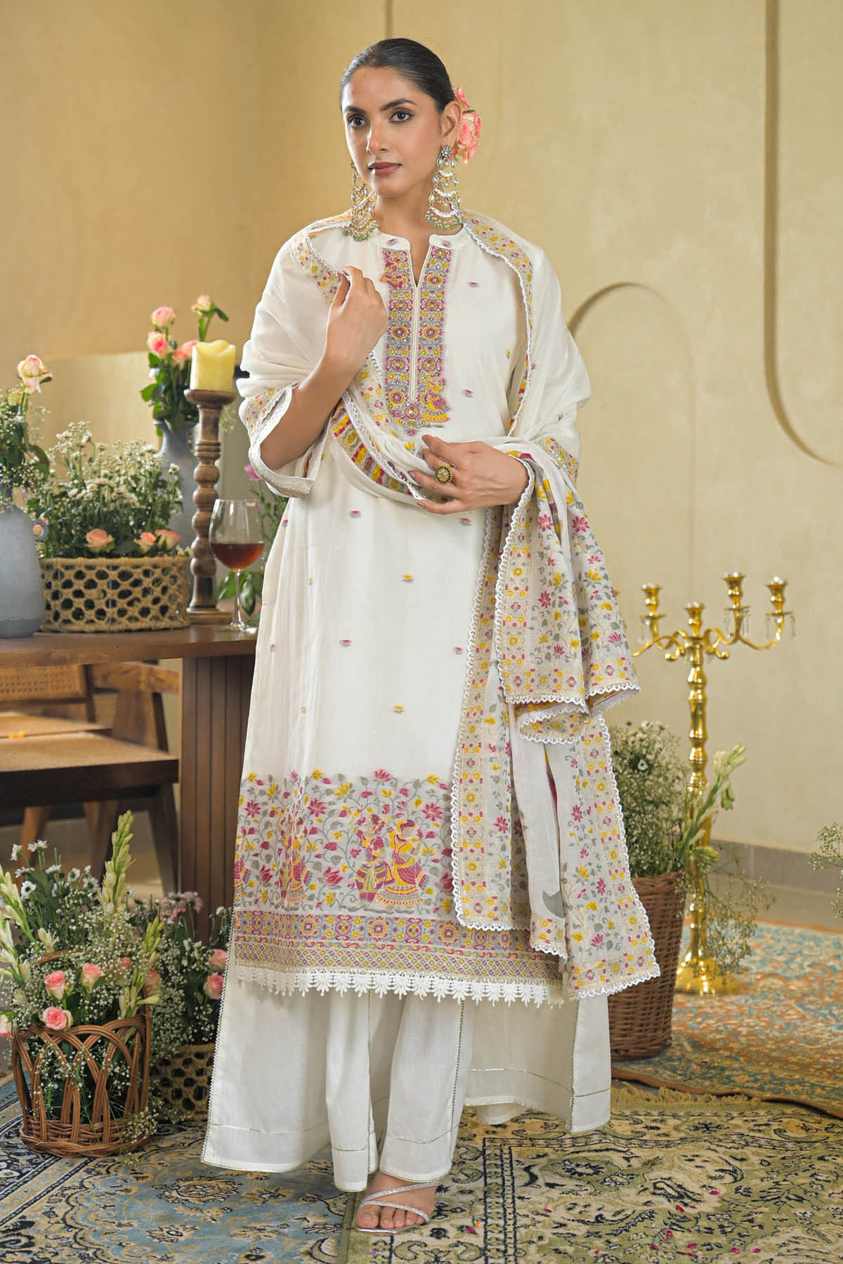 Woman in a white traditional outfit with floral patterns in an elegant indoor setting.
