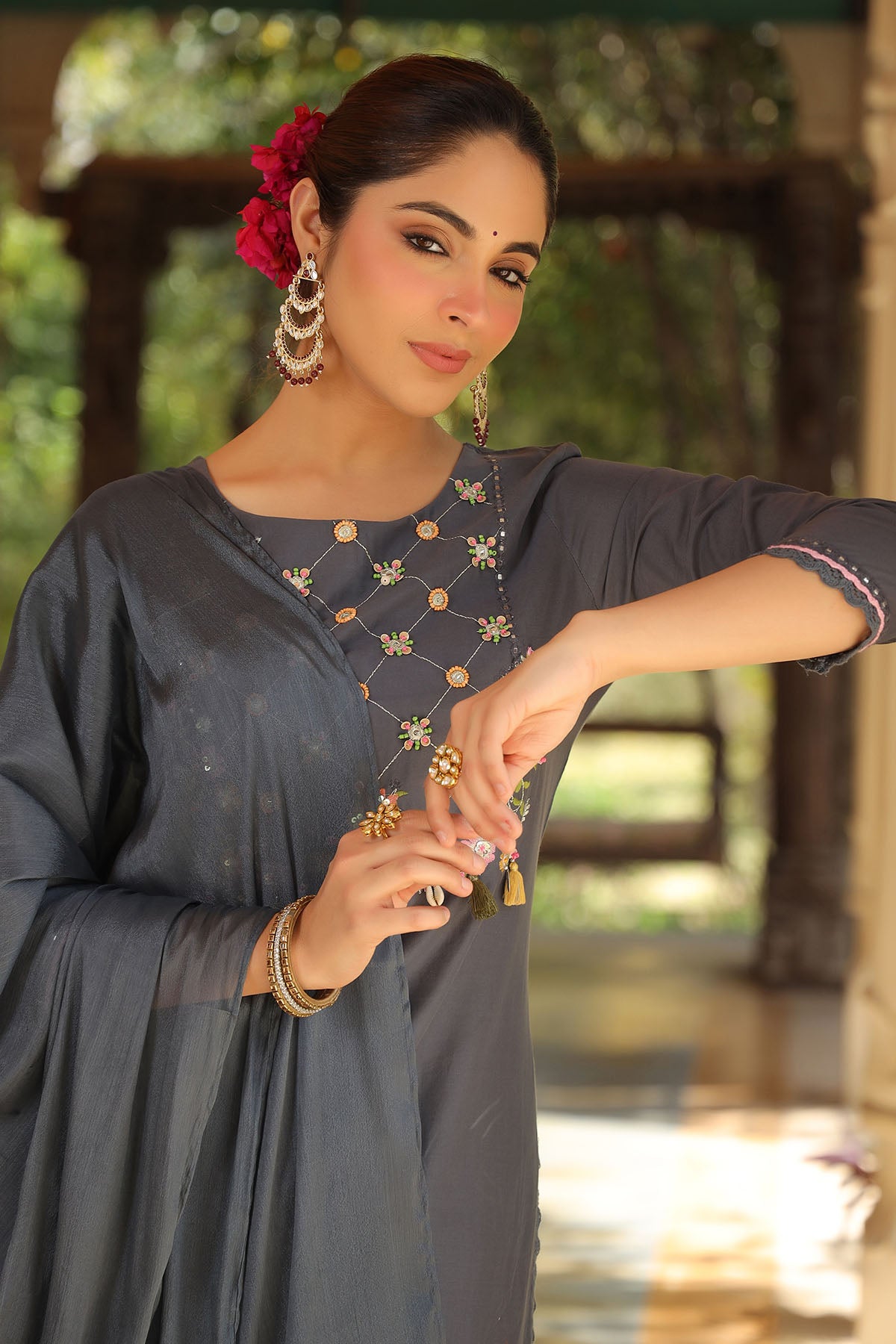 Woman in a dark gray traditional outfit with gold embroidery, standing outdoors.