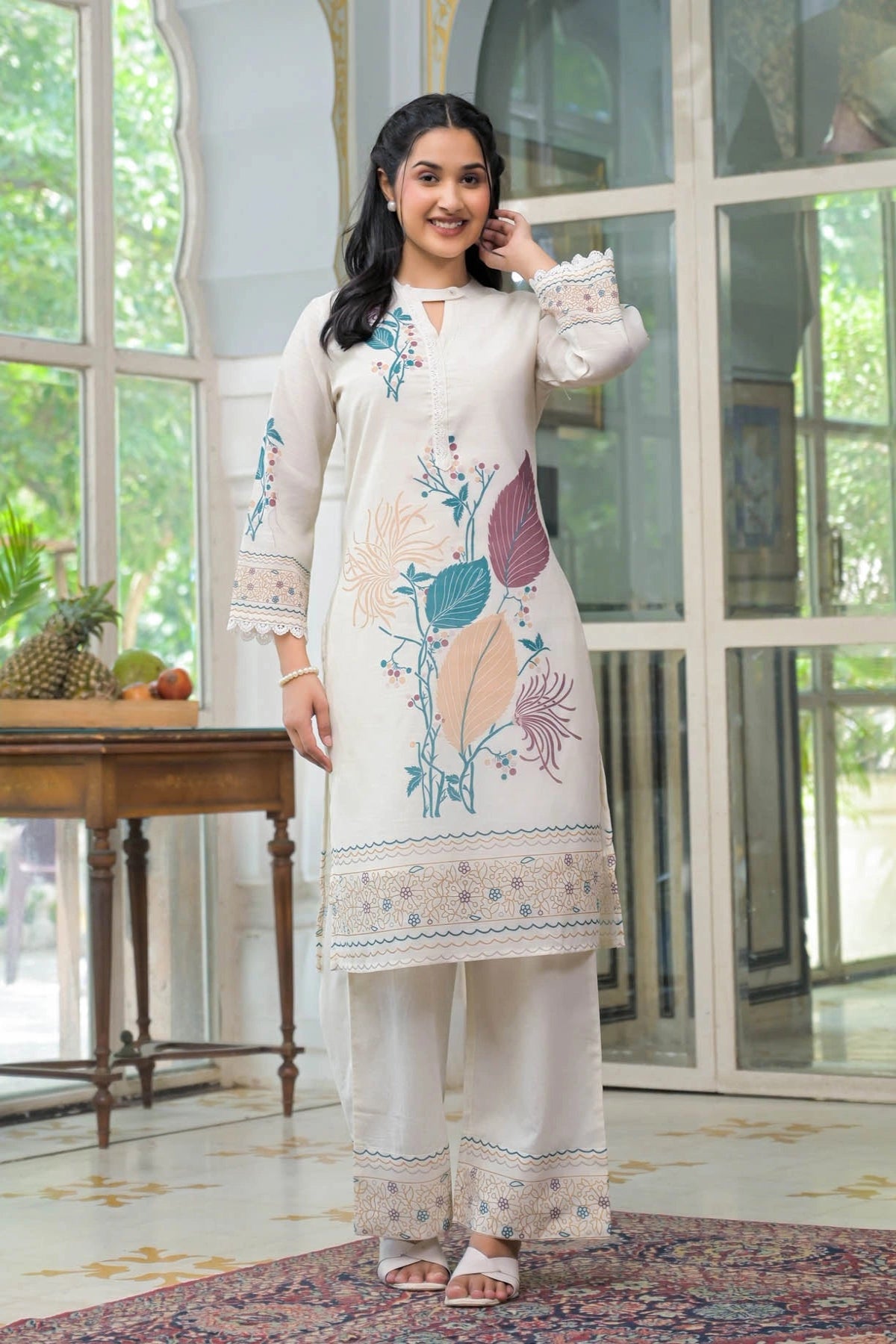 Woman wearing a white embroidered outfit in a bright room with large windows.
