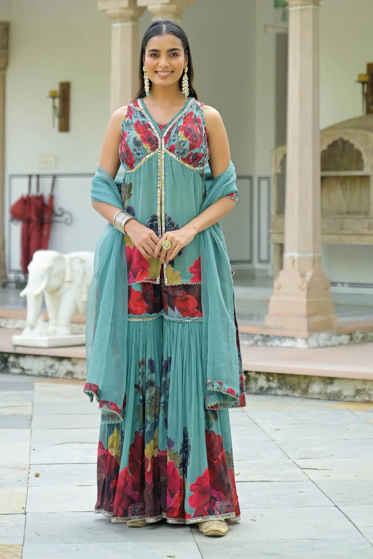 Woman wearing a teal and floral dress standing in an outdoor setting.