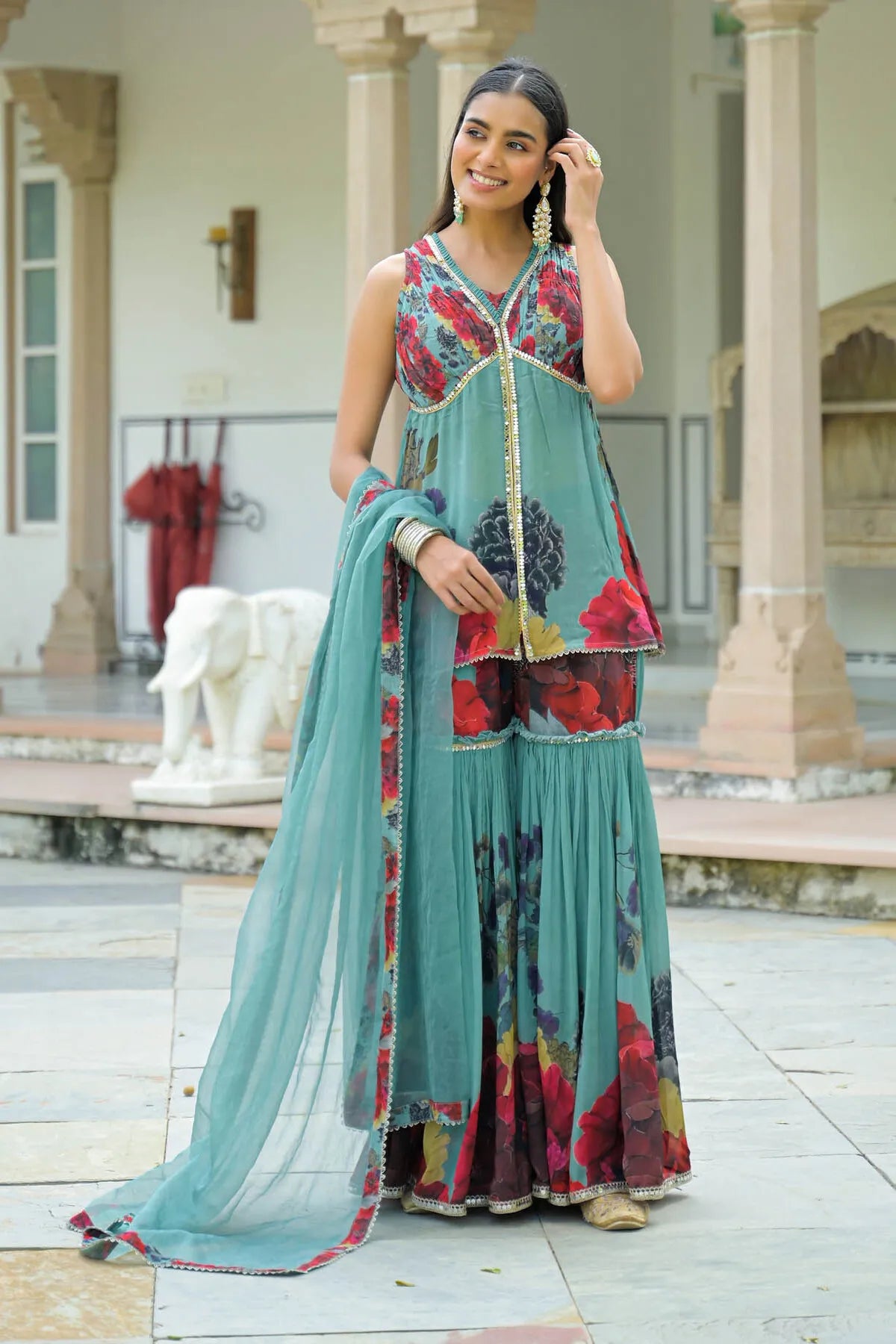 Woman in a colorful traditional outfit standing in front of a building with columns.