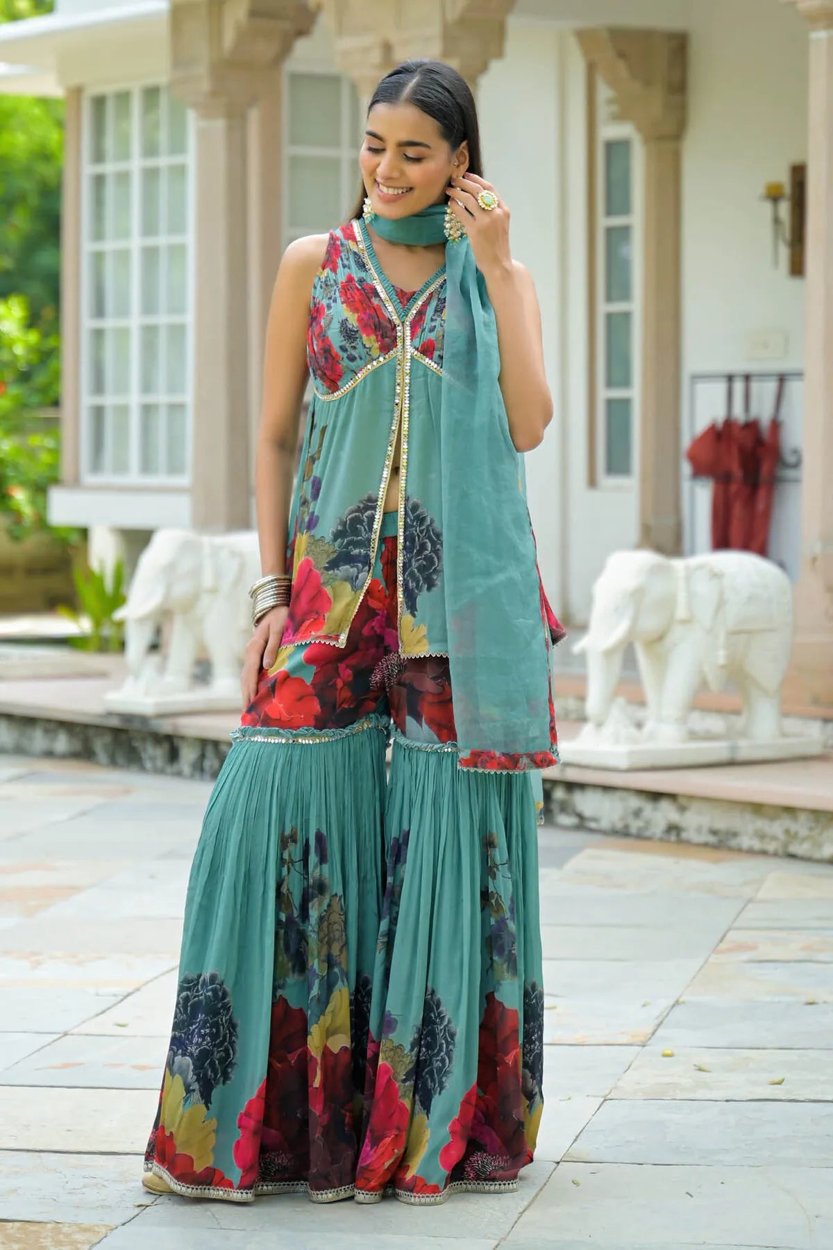 Woman in a colorful traditional outfit standing outdoors with decorative elements in the background.