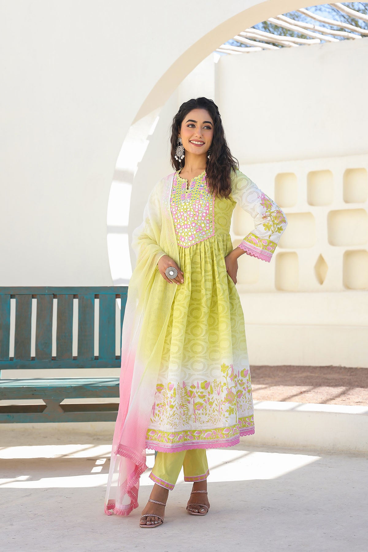 Woman in a light green traditional outfit with pink dupatta standing in a bright outdoor setting.