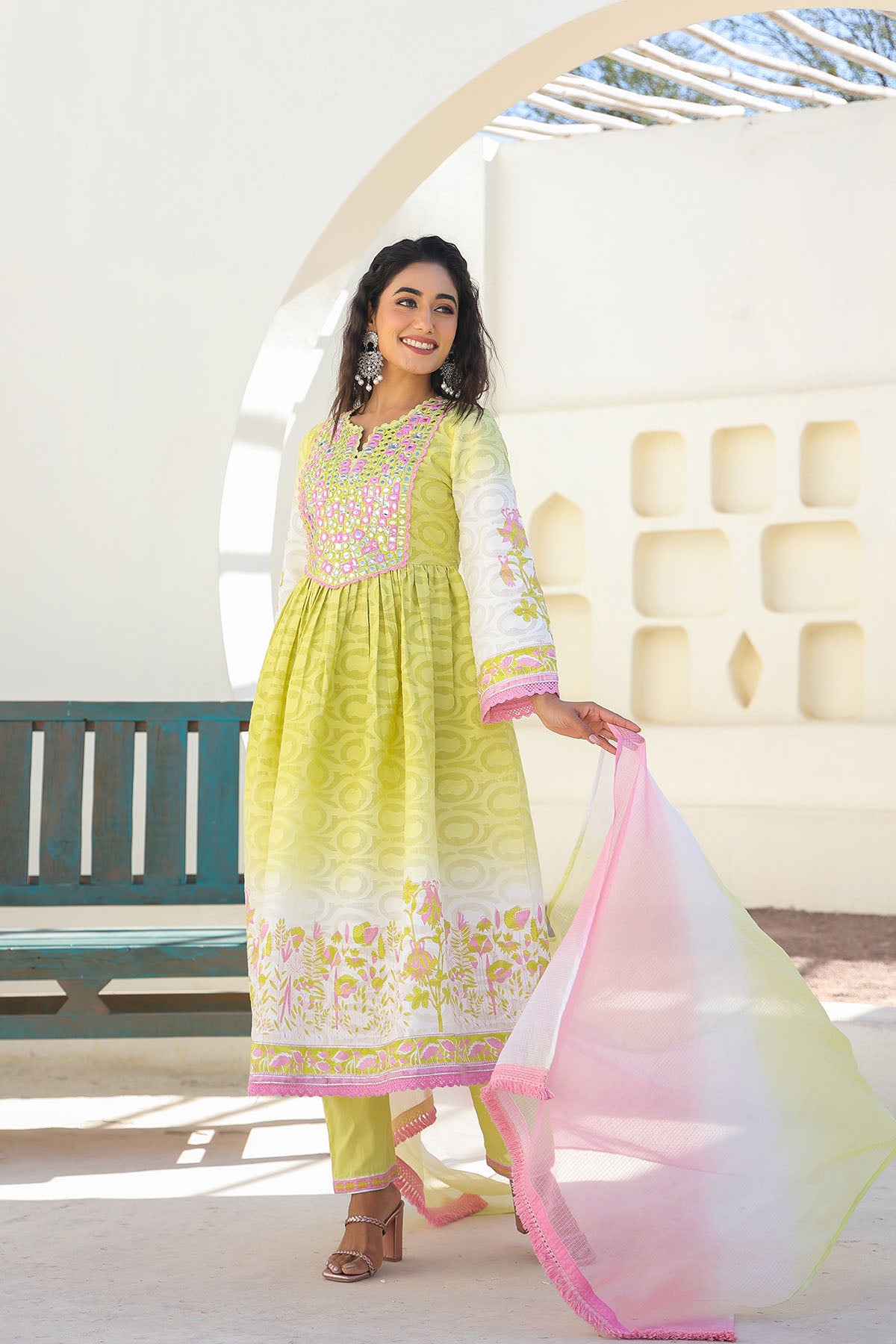 Woman in a traditional outfit with a light green and pink dress, standing in a bright indoor setting.