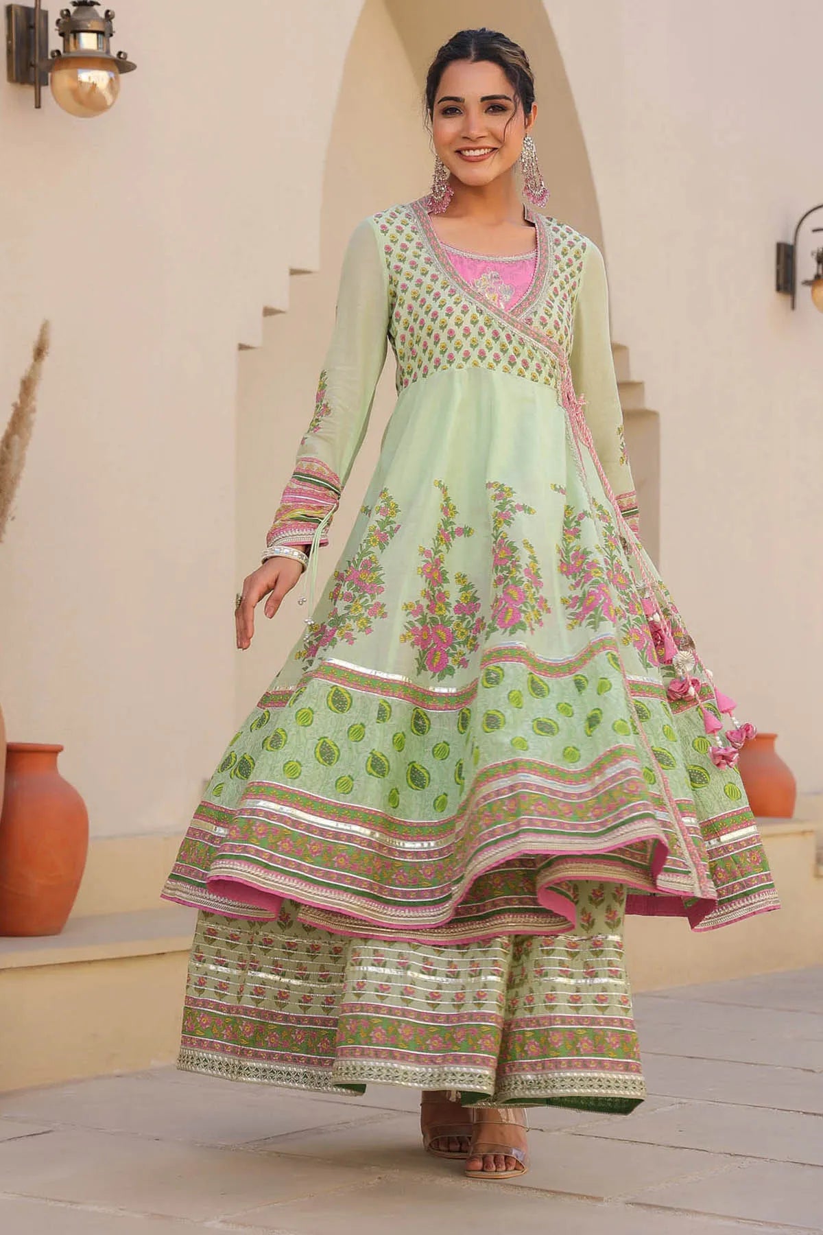Woman wearing a green and pink traditional outfit with floral patterns indoors.