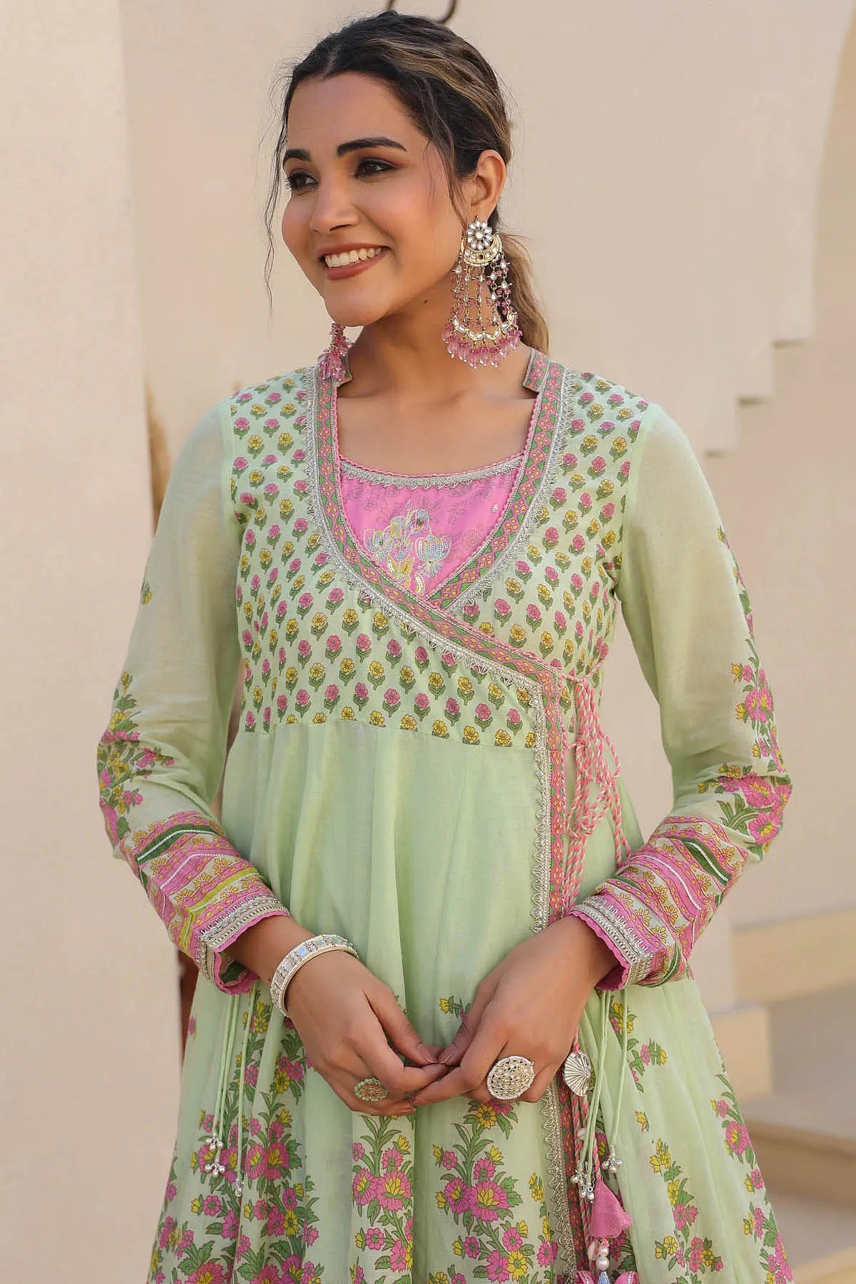 Woman wearing a light green traditional outfit with pink and floral patterns, smiling outdoors.