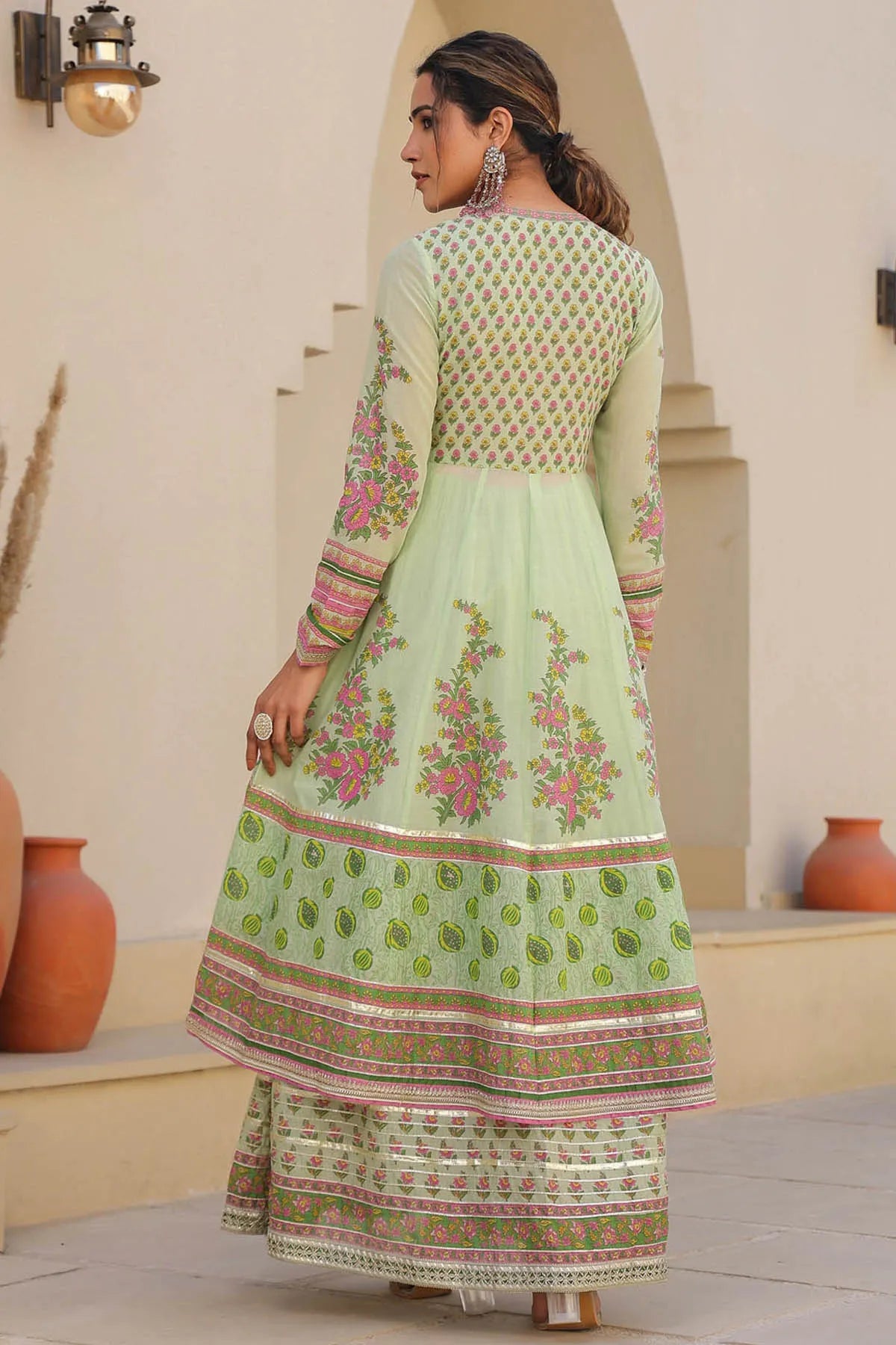 Woman wearing a light green traditional outfit with floral patterns in an outdoor setting.