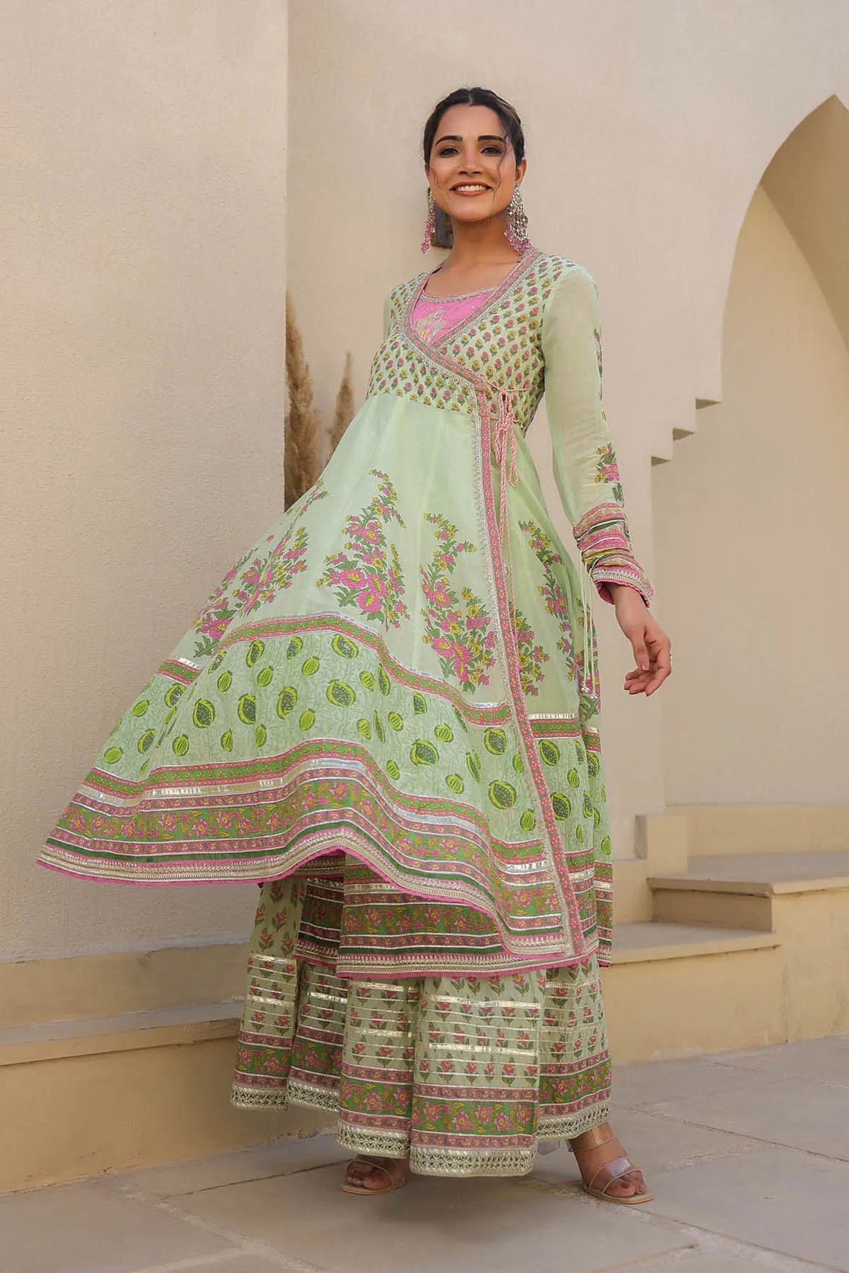 Woman wearing a traditional green and pink embroidered outfit in an indoor setting.