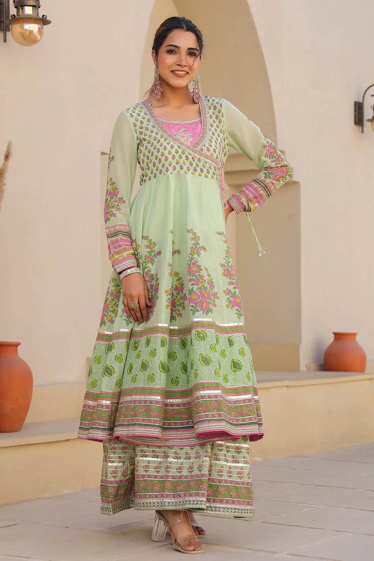 Woman wearing a light green traditional outfit with floral patterns in an indoor setting.