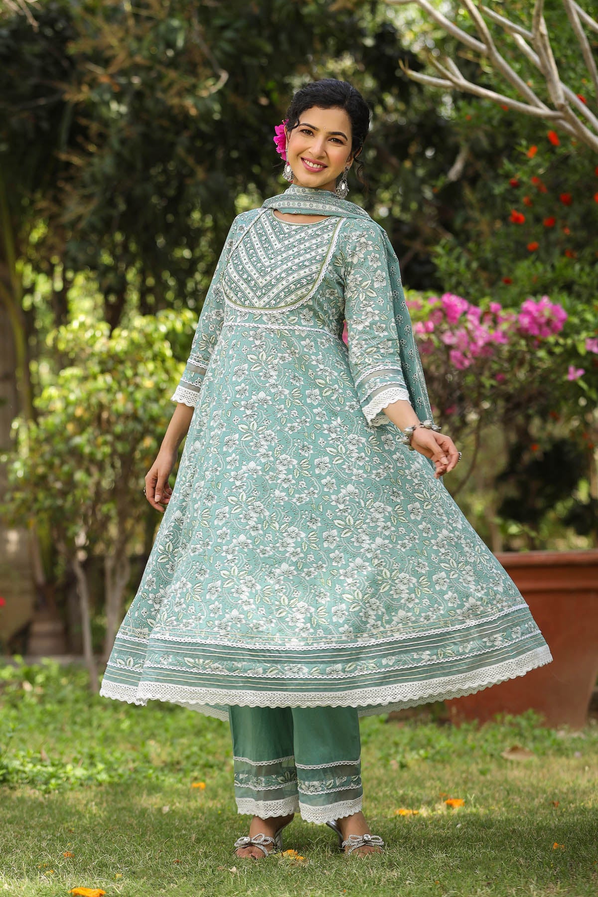 Woman wearing a light green traditional outfit with floral patterns in an outdoor setting.