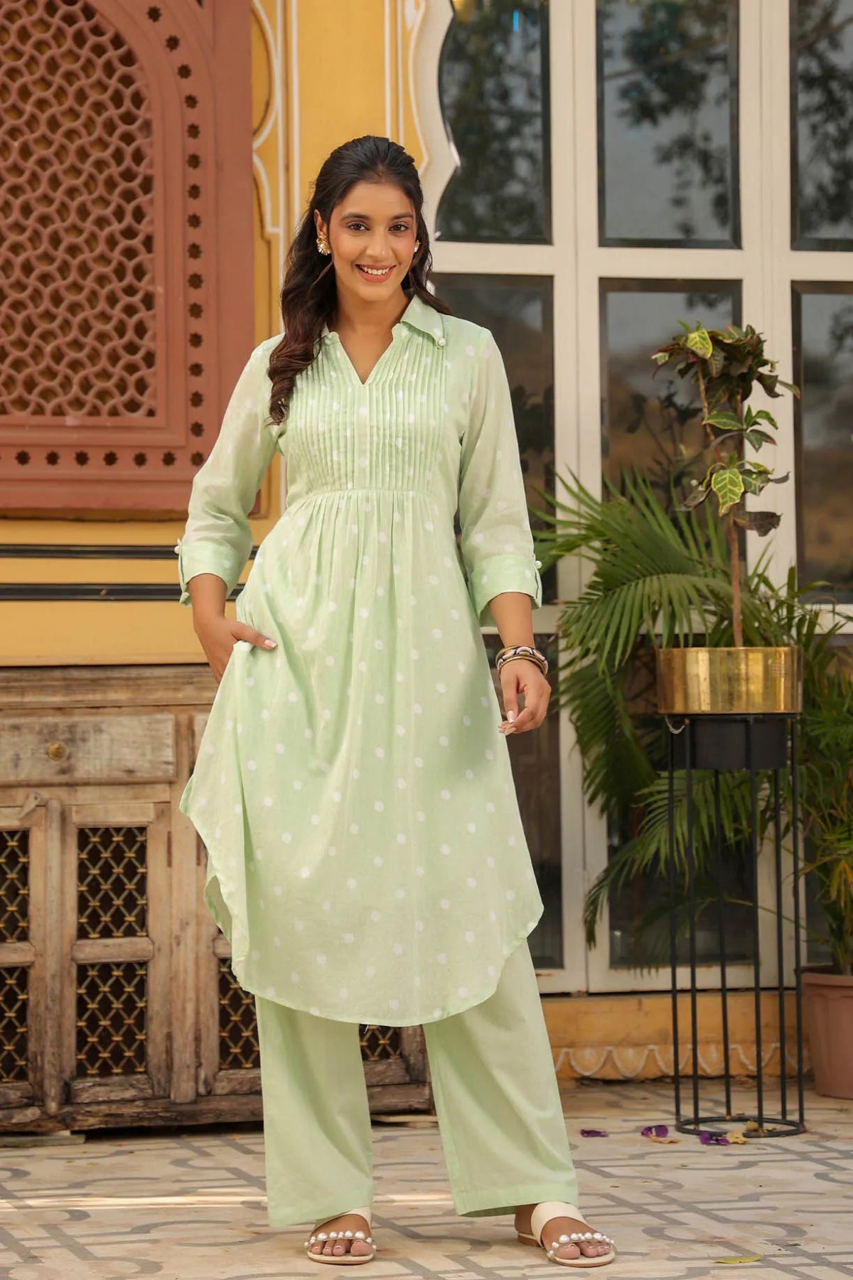Woman wearing a light green traditional outfit standing in front of a decorative wall.