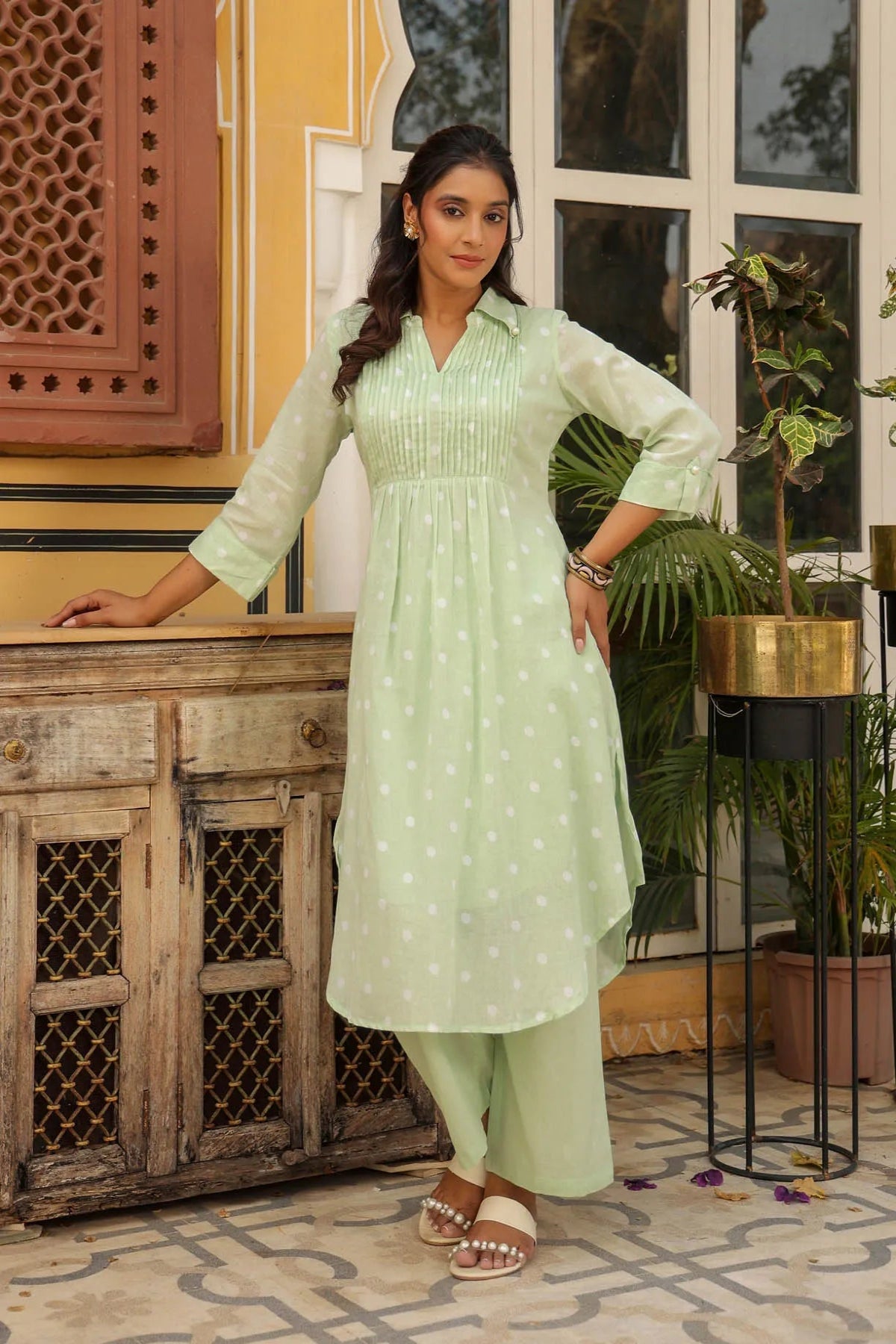 Woman in a light green traditional outfit standing in a decorative indoor setting.