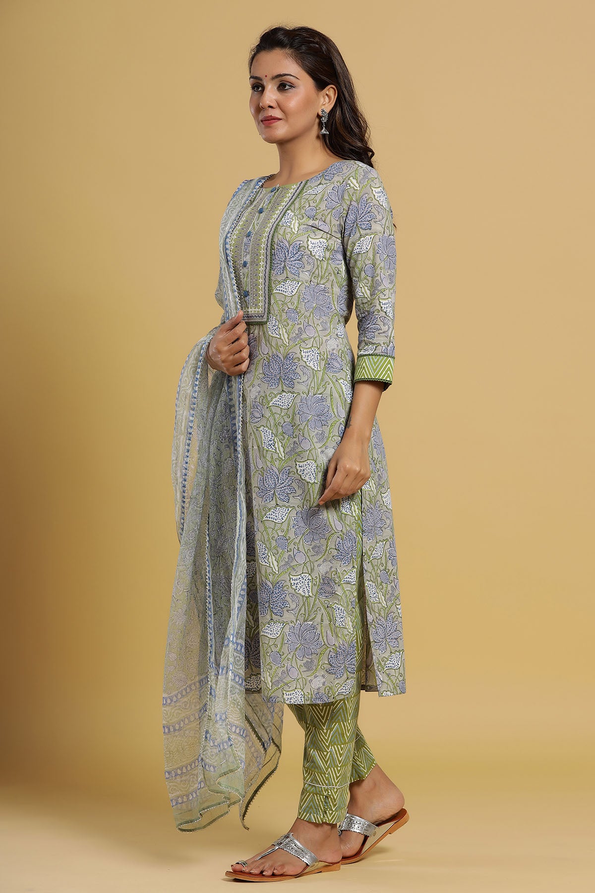 Woman wearing a green and white floral kurta with matching pants and dupatta on a beige background