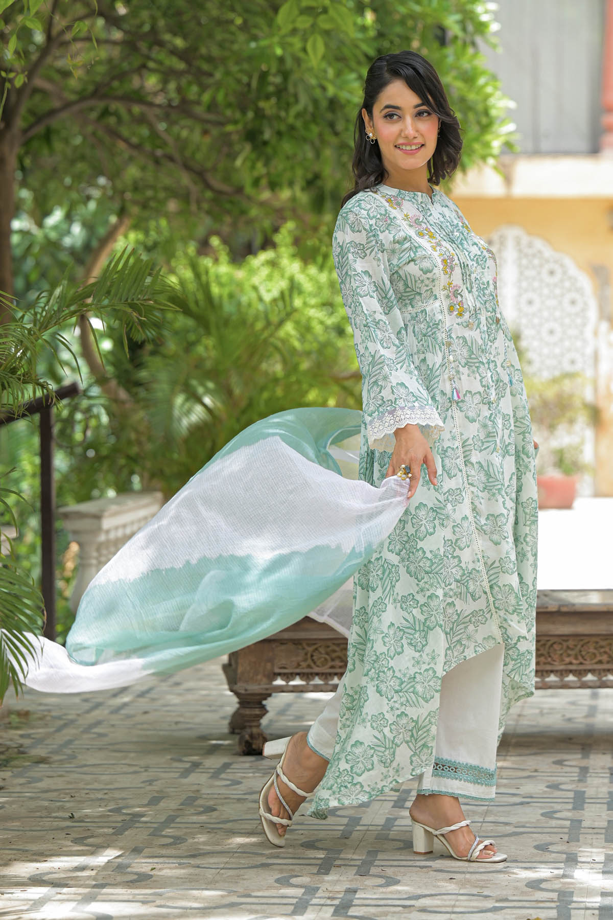 Woman in a light green and white traditional outfit with a flowing shawl outdoors.