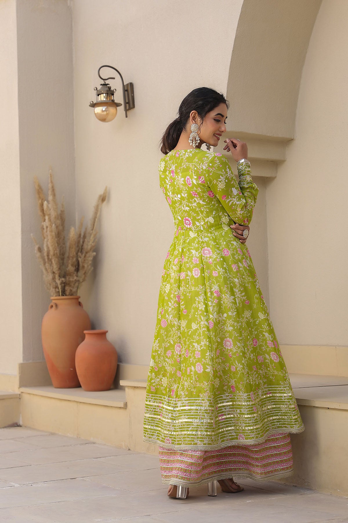 Woman in a green floral dress standing in an outdoor setting with decorative vases.