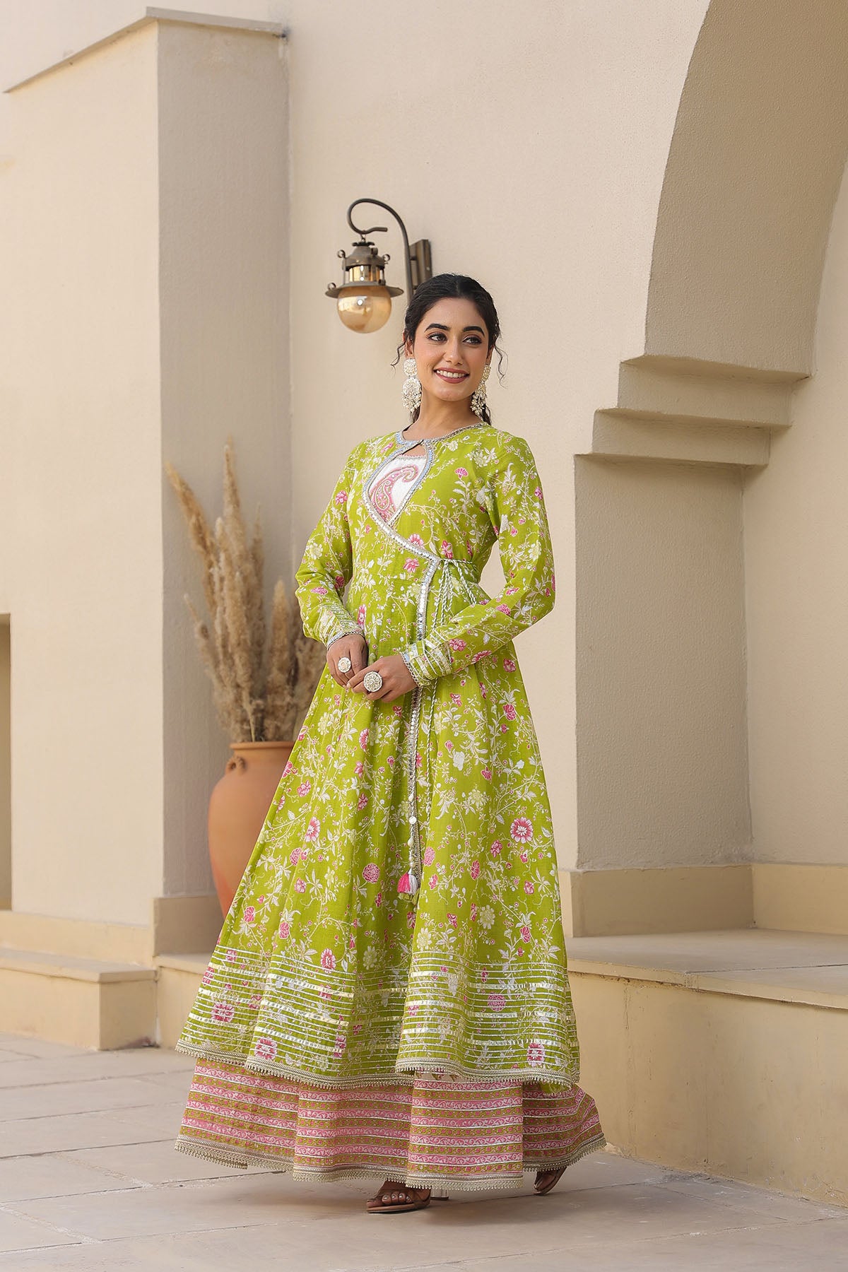Woman in a green floral dress standing in an outdoor setting with beige walls and steps.
