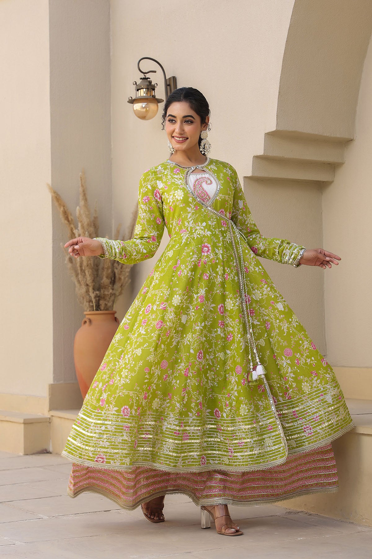Woman wearing a green floral traditional outfit standing in an outdoor setting.