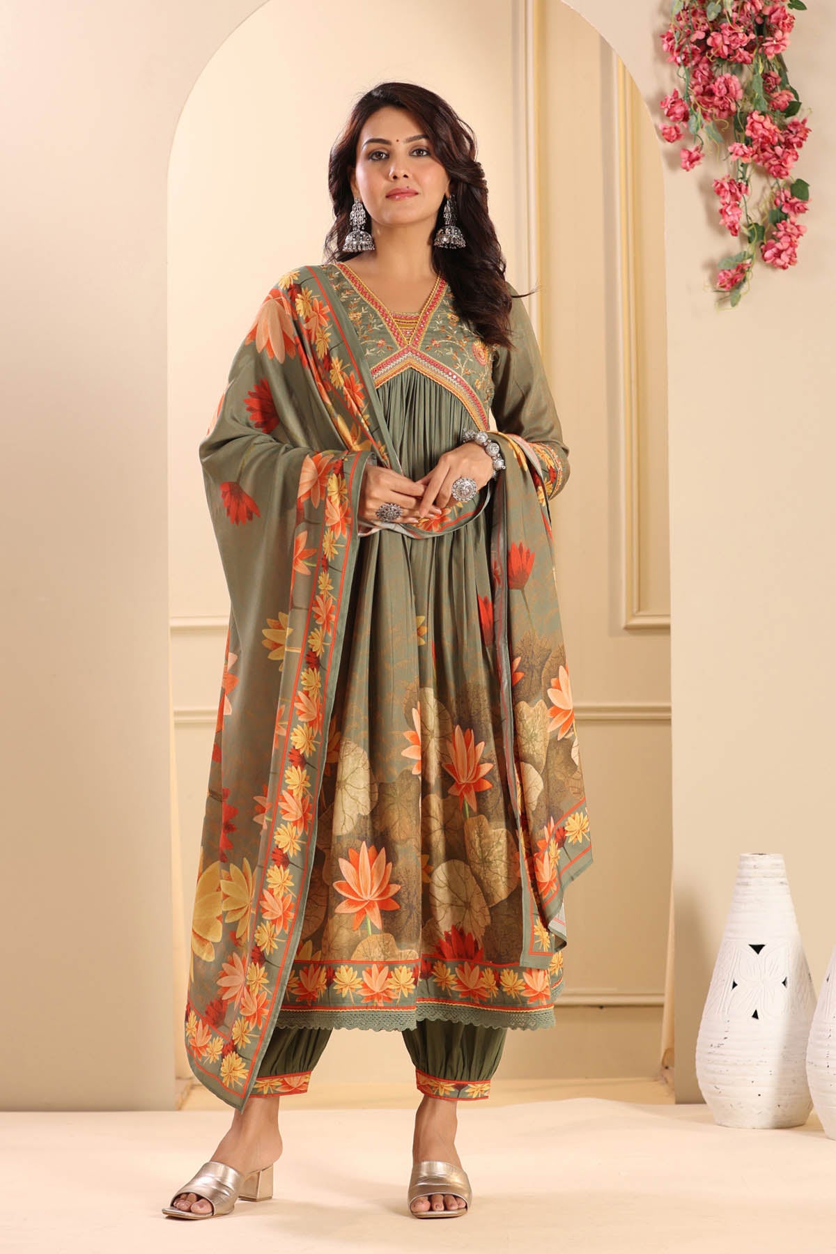 Woman wearing a floral dress with a matching dupatta in a decorated room.