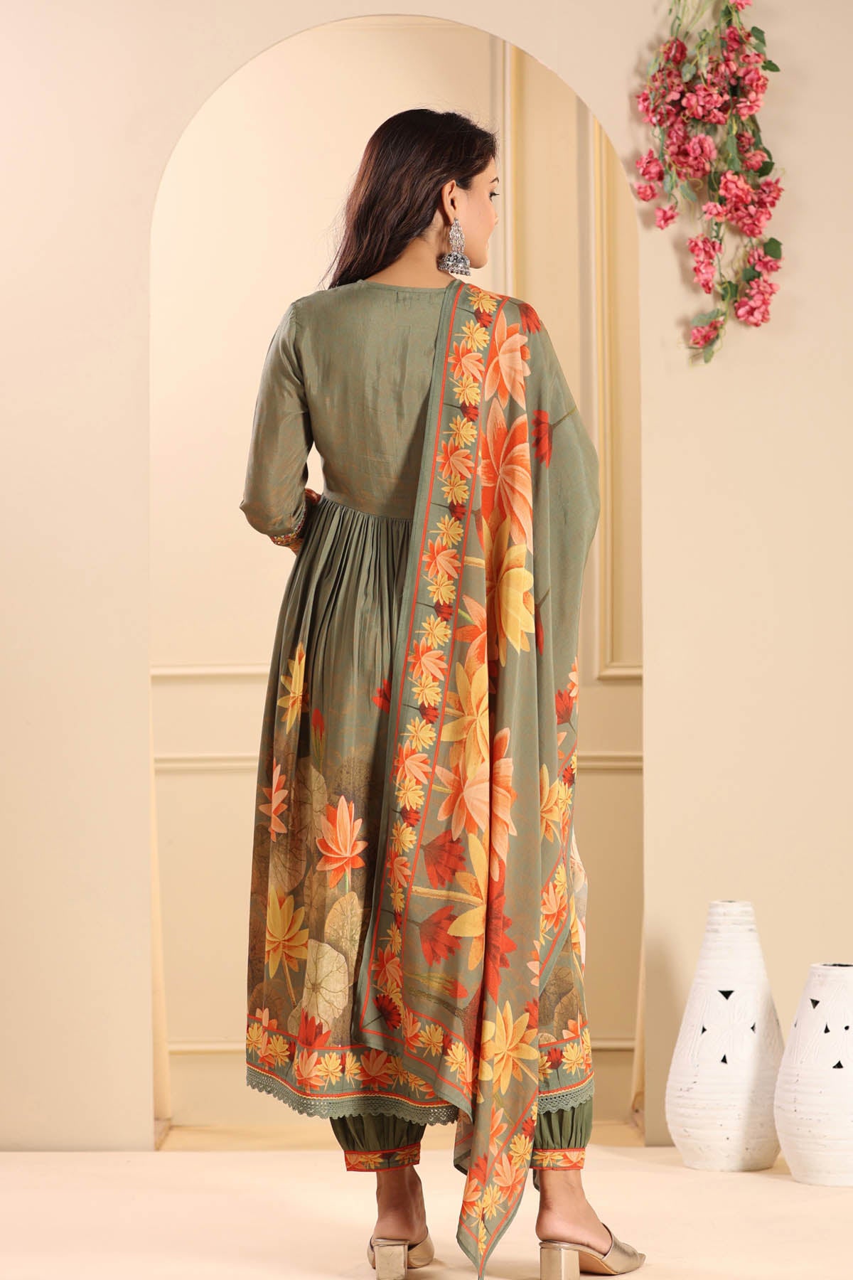 Woman wearing a green dress with a floral dupatta in a decorated room.