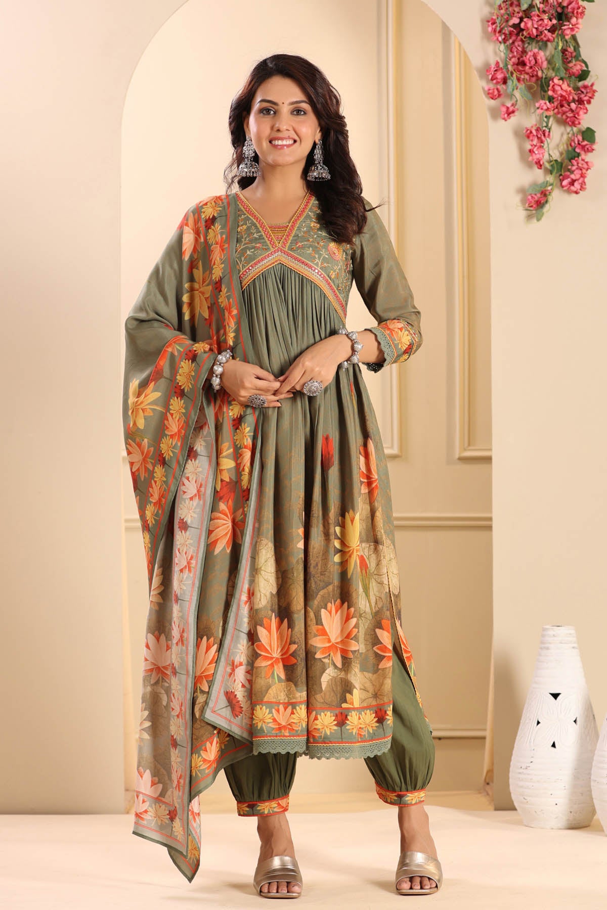 Woman wearing a green and orange floral dress with a matching dupatta in a decorated room.