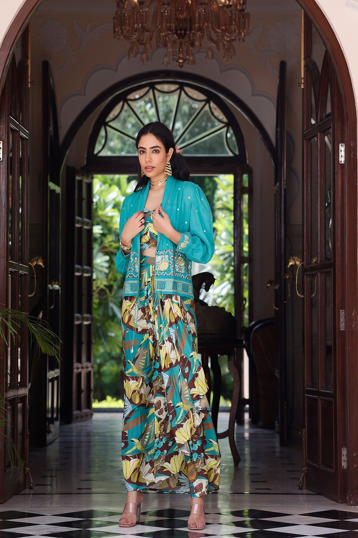 Woman in a turquoise outfit with floral patterns standing in a decorated hallway.