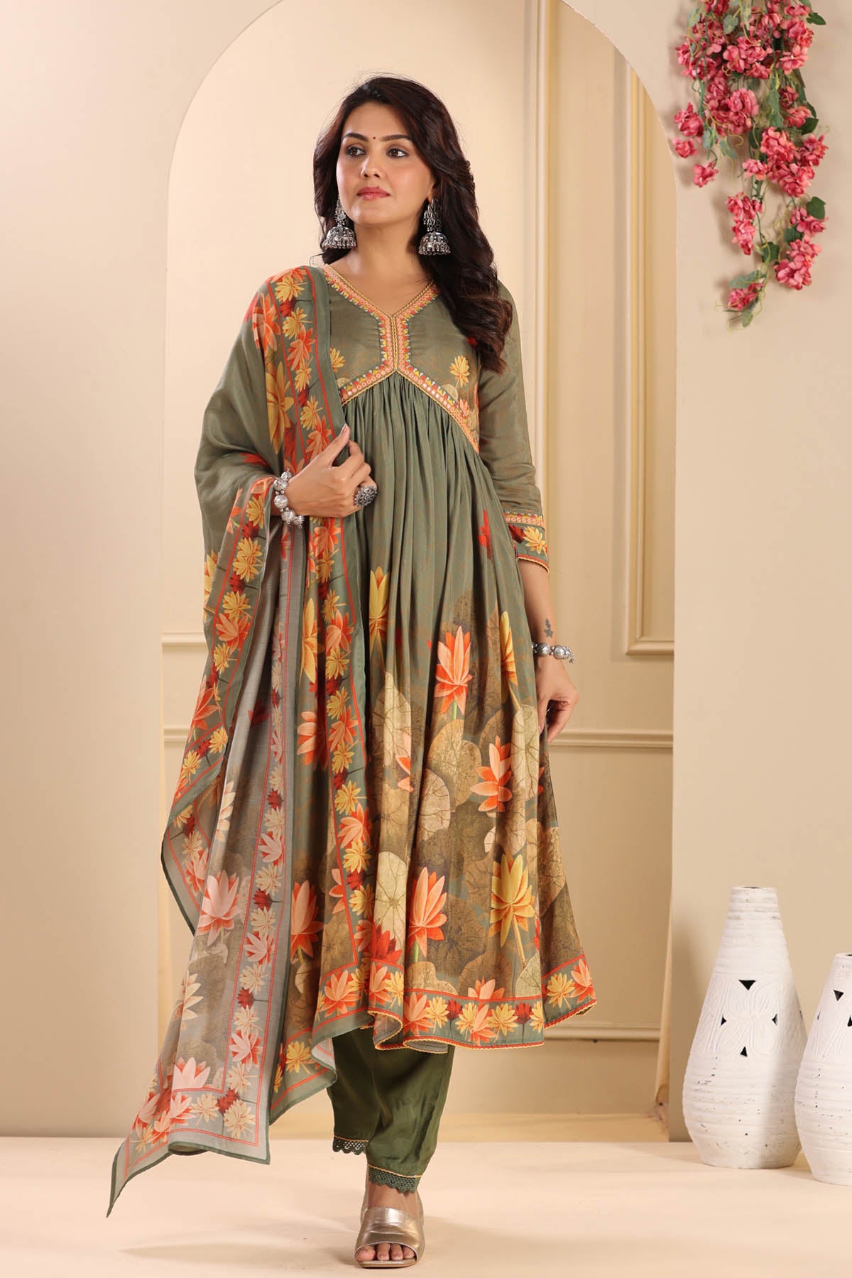 Woman wearing a green traditional outfit with a floral dupatta in a decorated room.