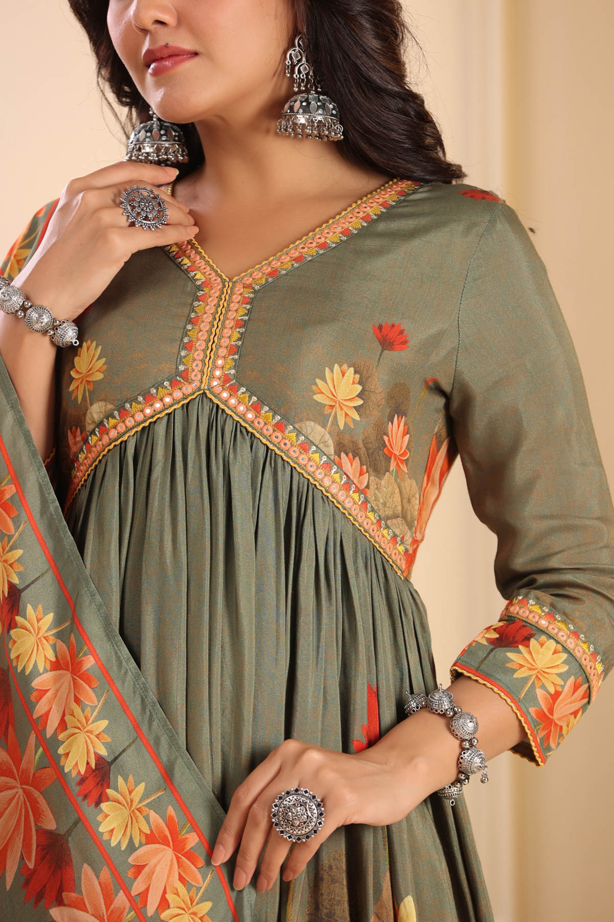 Woman wearing a green embroidered dress with floral patterns, holding a matching dupatta.