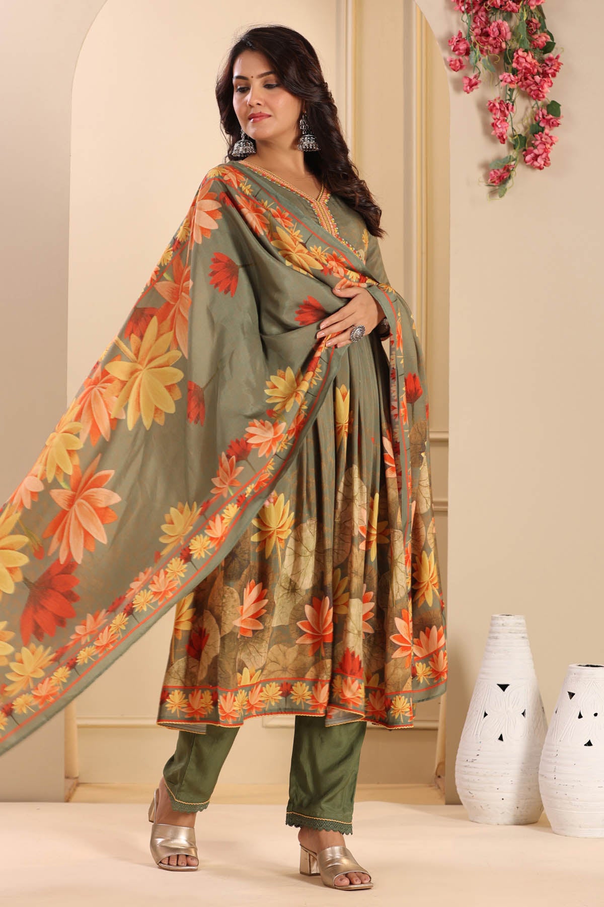 Woman wearing a floral dress with a matching dupatta in a decorated room.