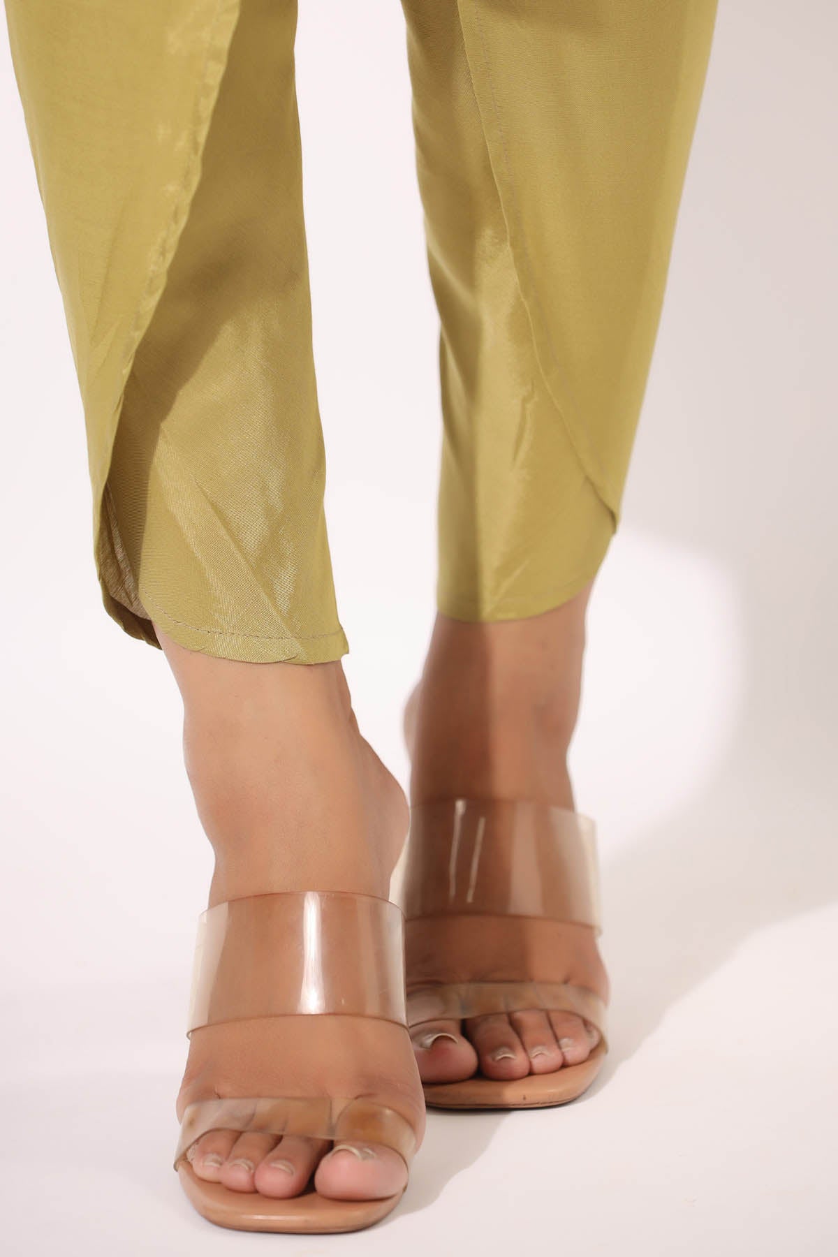 Clear high-heeled sandals worn with green pants on a white background