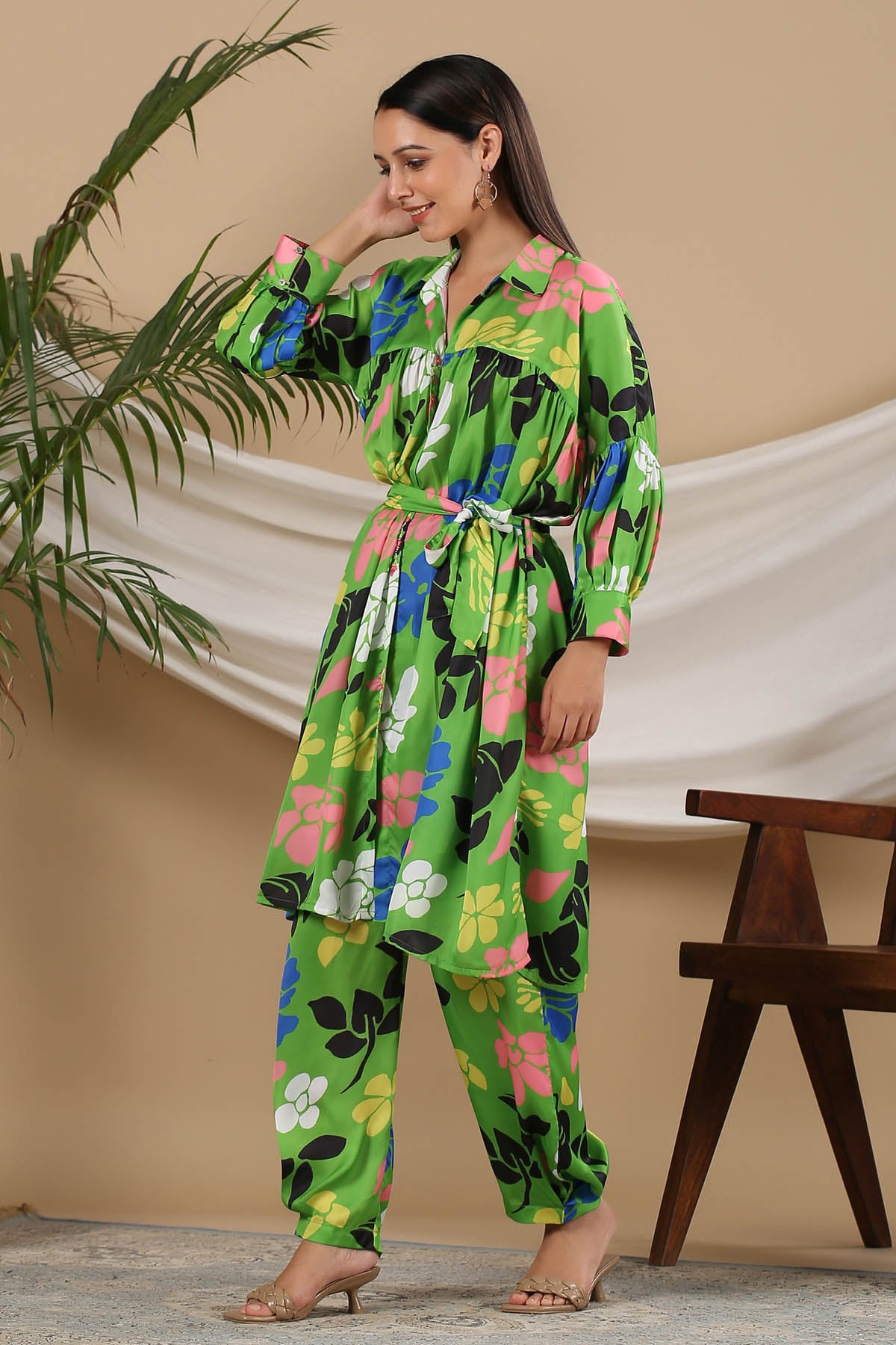 Woman wearing a colorful floral jumpsuit standing next to a plant and wooden bench.