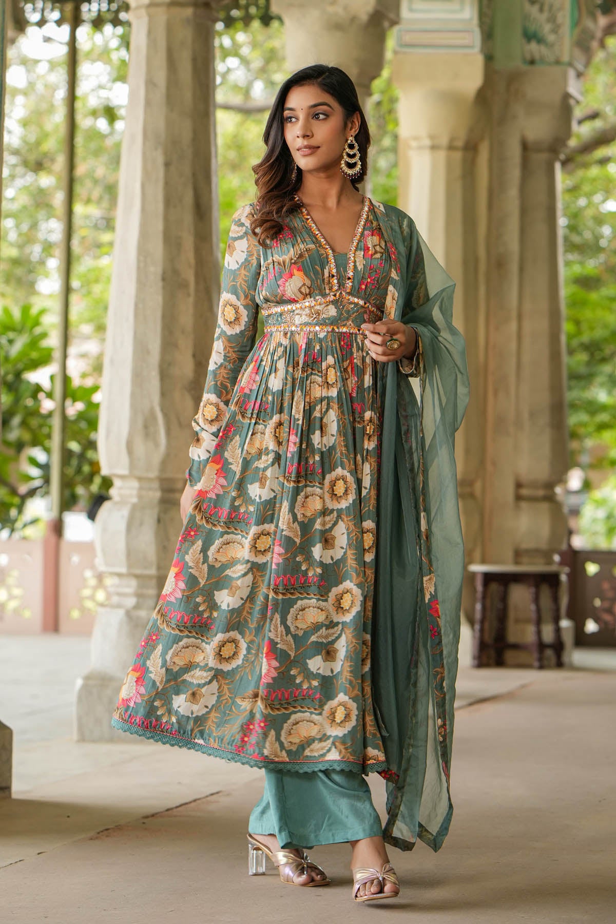 Woman in a floral dress standing in an outdoor setting with columns and greenery.