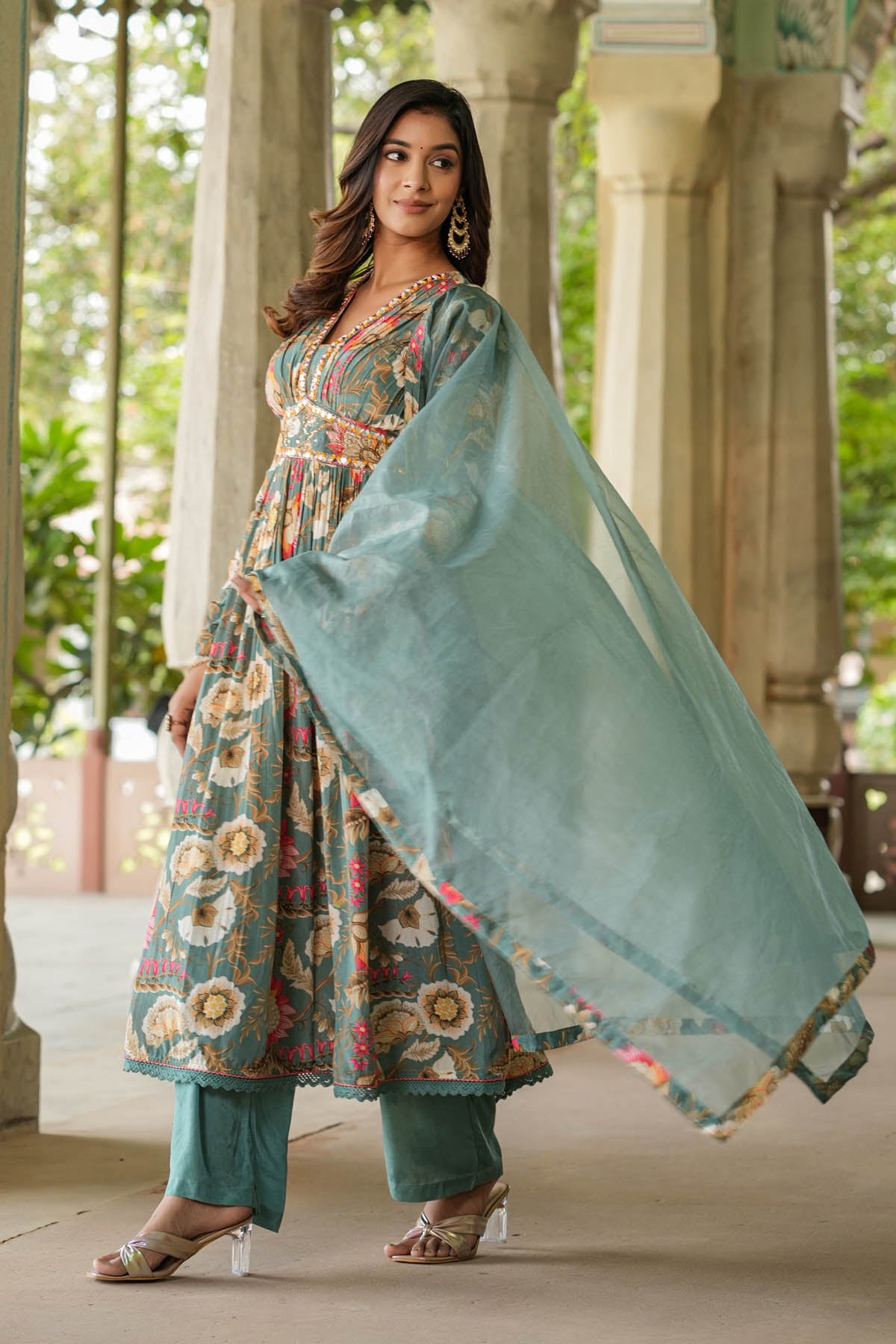 Woman in a floral dress with a light blue dupatta standing outdoors.