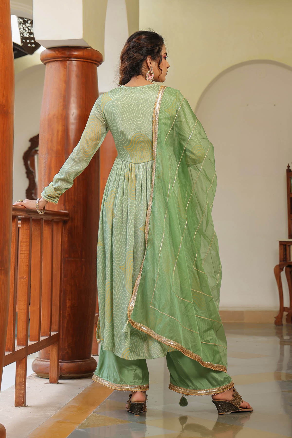 Woman in a green traditional outfit standing in a room with wooden furniture.