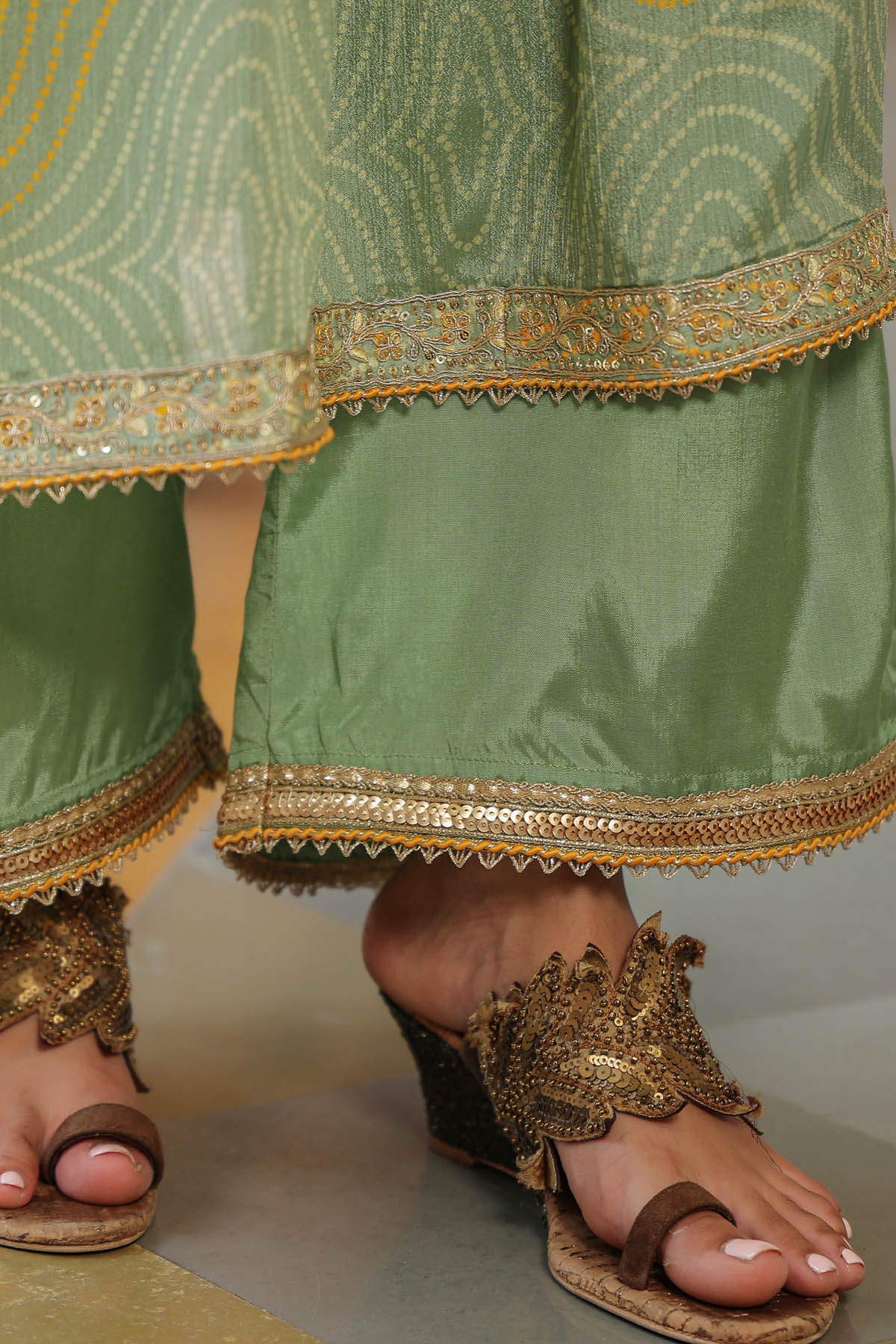 Green traditional outfit with gold embroidery and sandals on a neutral background