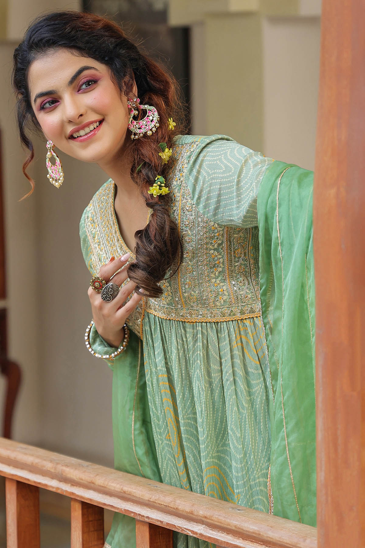 Woman in a green traditional outfit with floral hair accessories indoors.