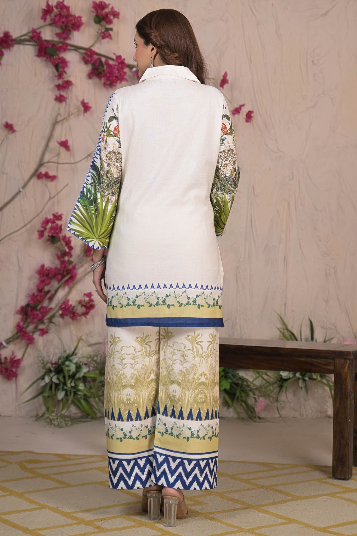 Woman wearing a white traditional outfit with colorful patterns in a decorative setting.