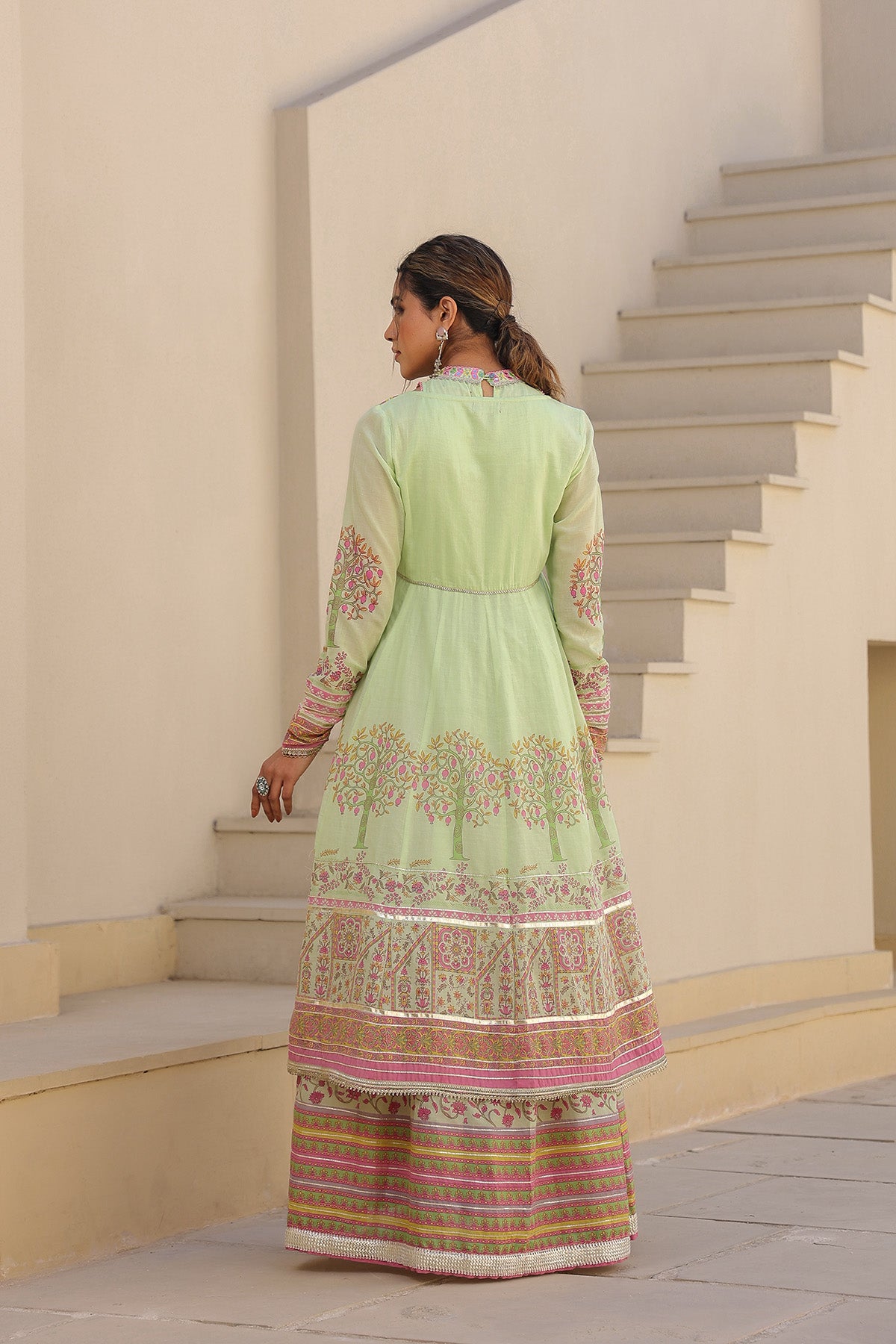 Woman in a light green traditional outfit standing on a staircase.
