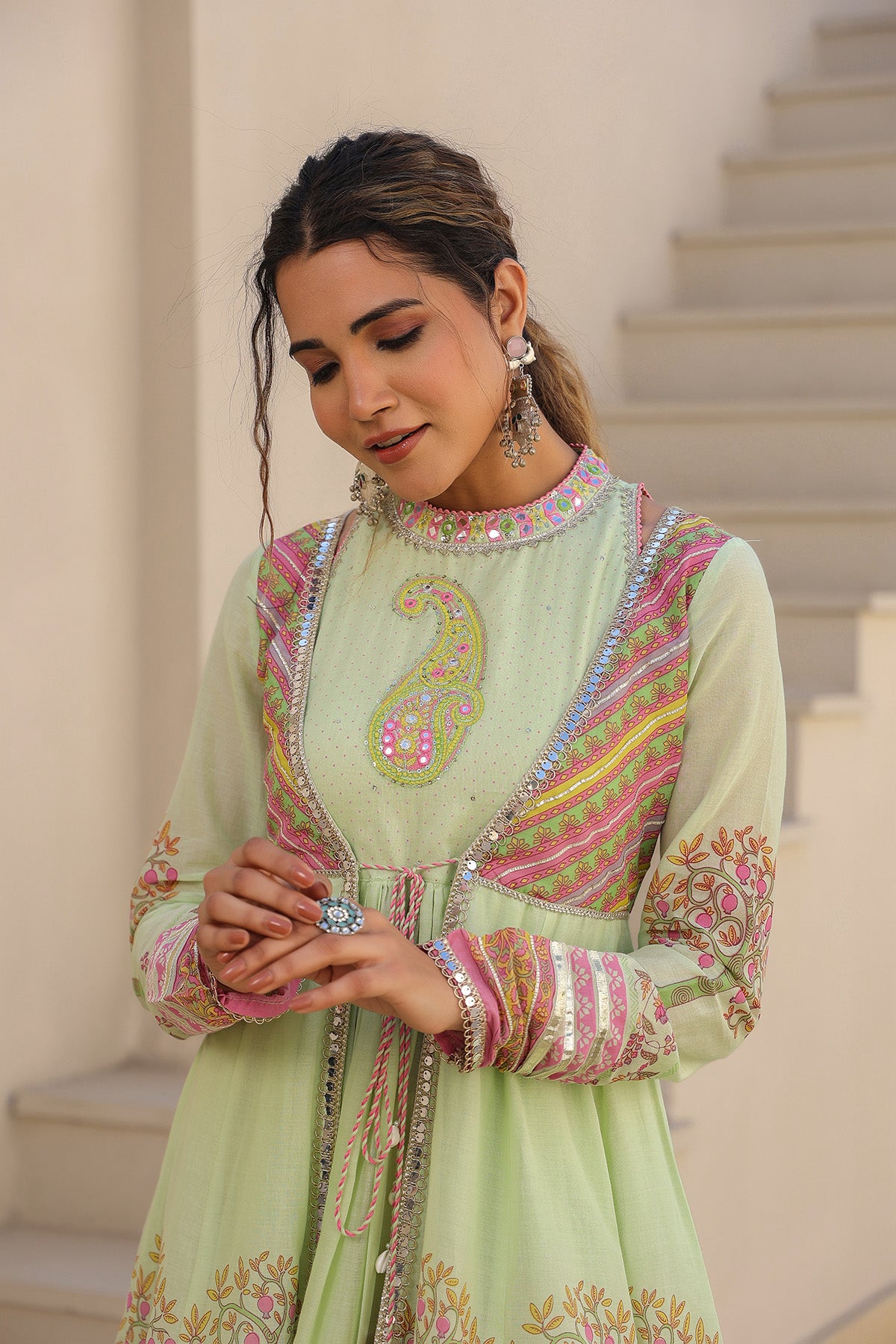 Woman in a light green traditional outfit with colorful embroidery standing on steps.