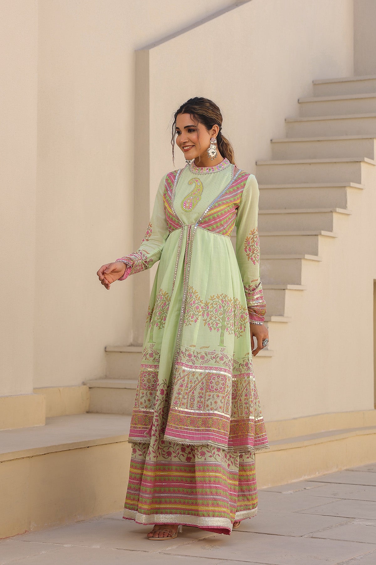 Woman in a light green traditional outfit with floral patterns standing on a staircase.