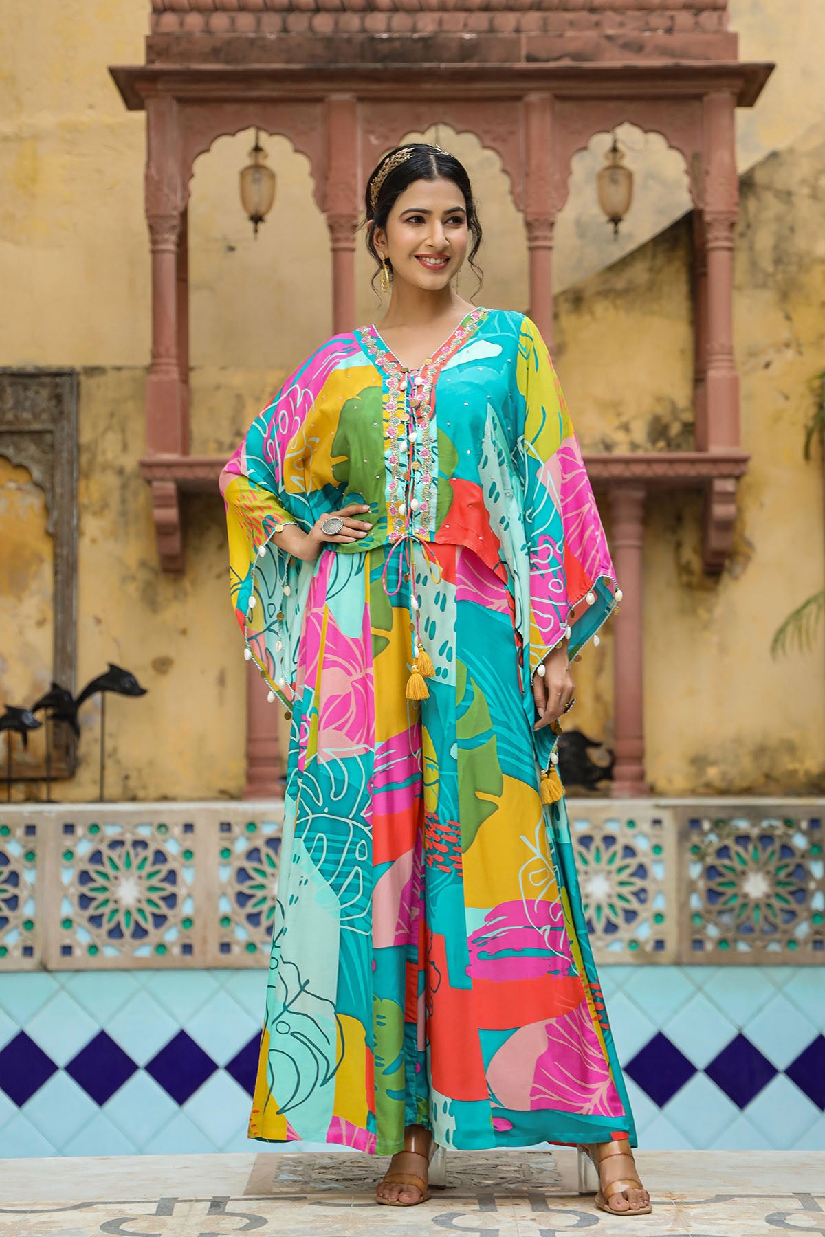 Woman in a colorful traditional outfit standing in front of a decorative wall.