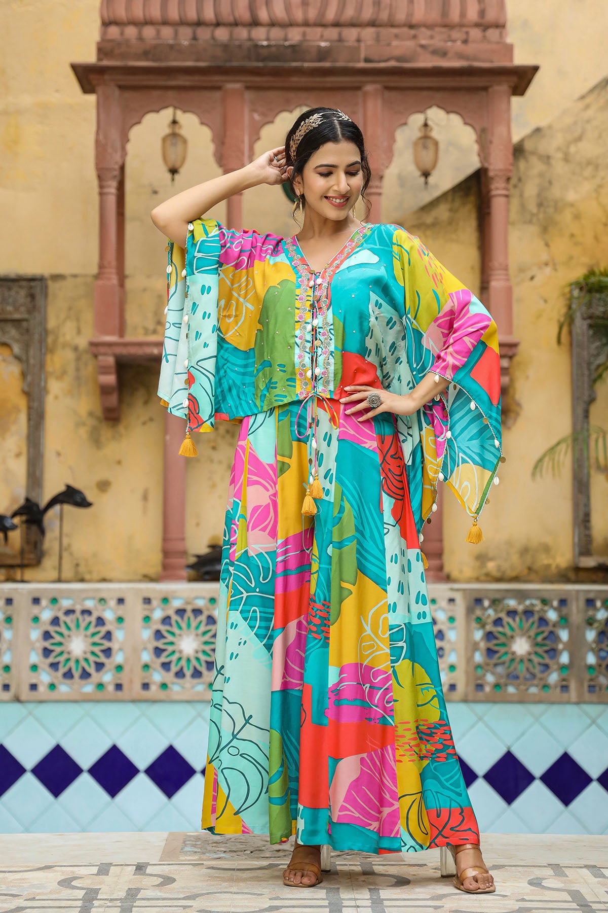 Woman in a colorful traditional outfit standing in front of a decorative wall.